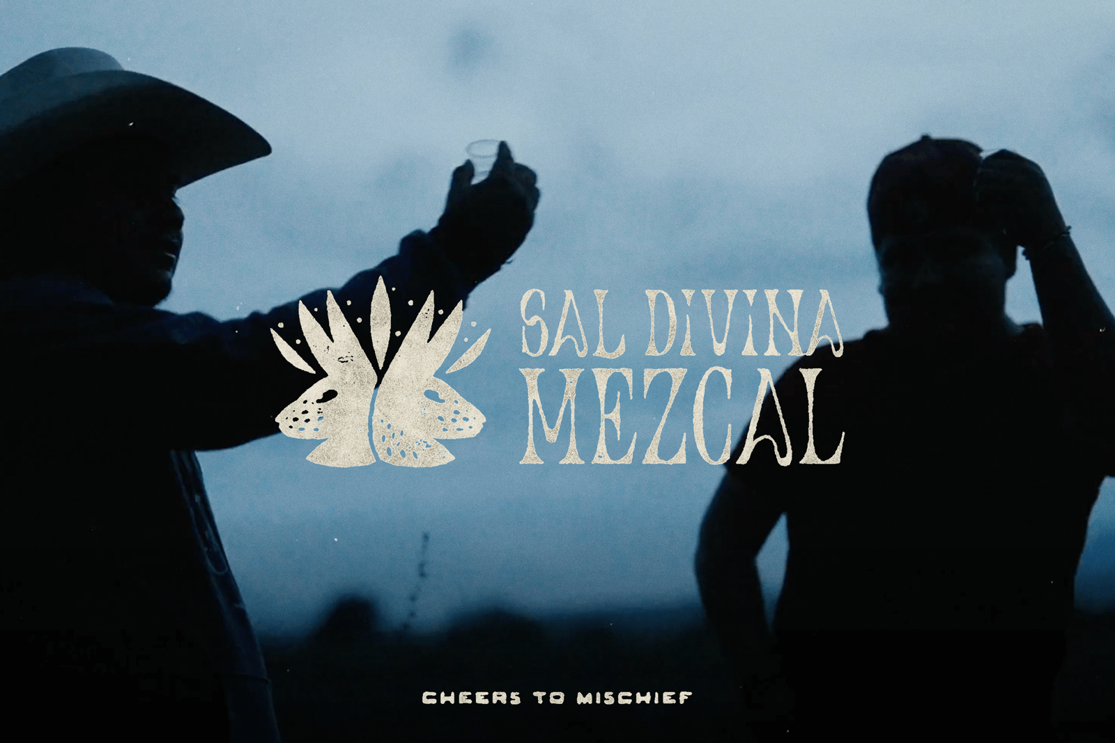 A silhouette of two Mezcaleros raising small glasses of Mezcal against the evening sky of Oaxaca.