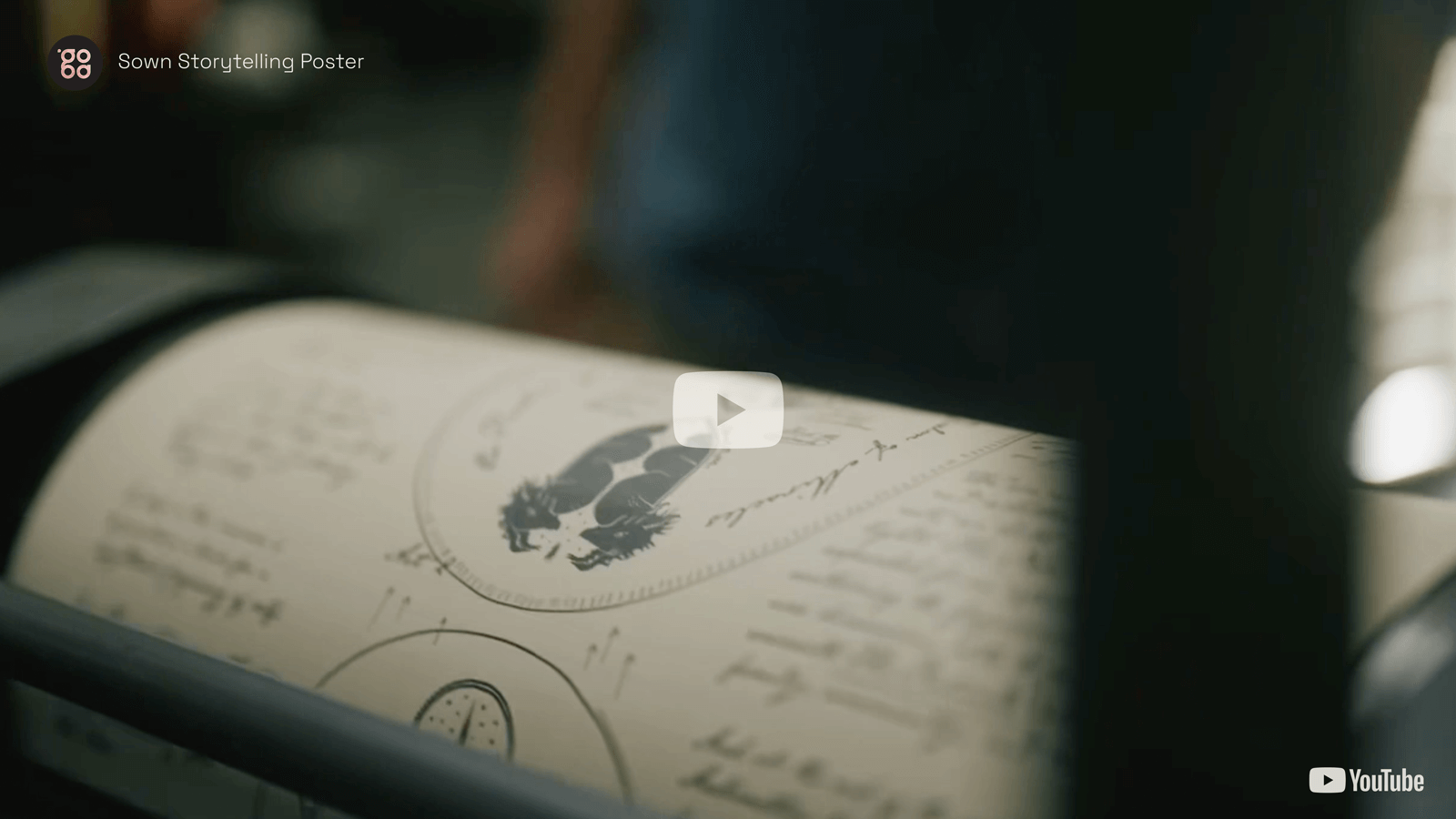 Close-up of a poster with handwritten notes and illustrations being actively printed on a large letterpress, softly lit and slightly blurred.