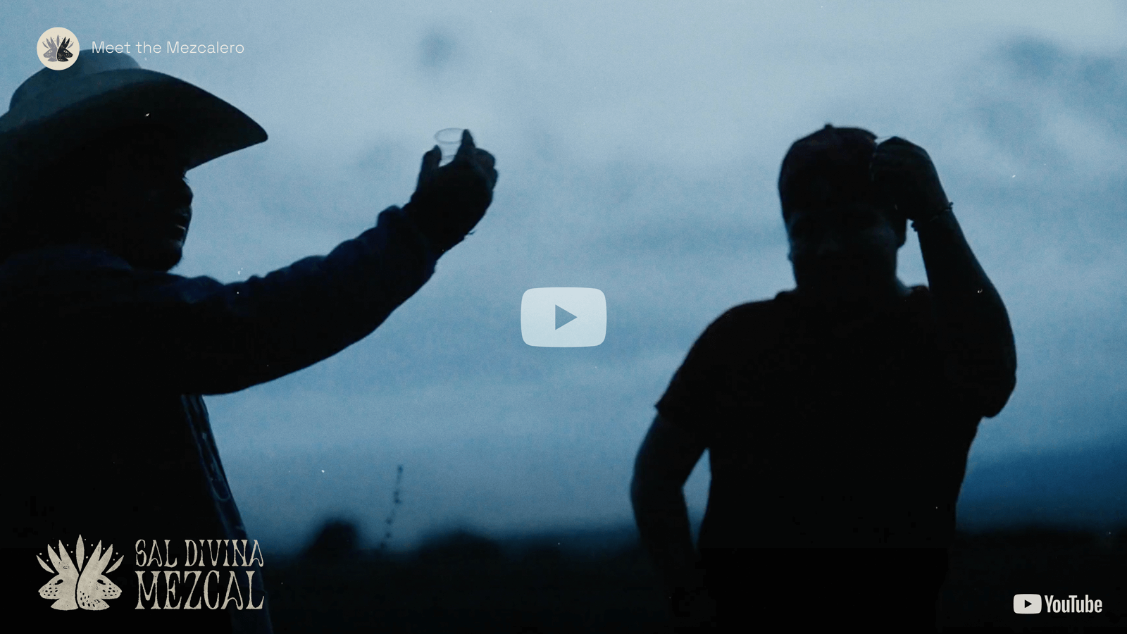A silhouette of two Mezcaleros raising small glasses of Mezcal against the evening sky of Oaxaca.