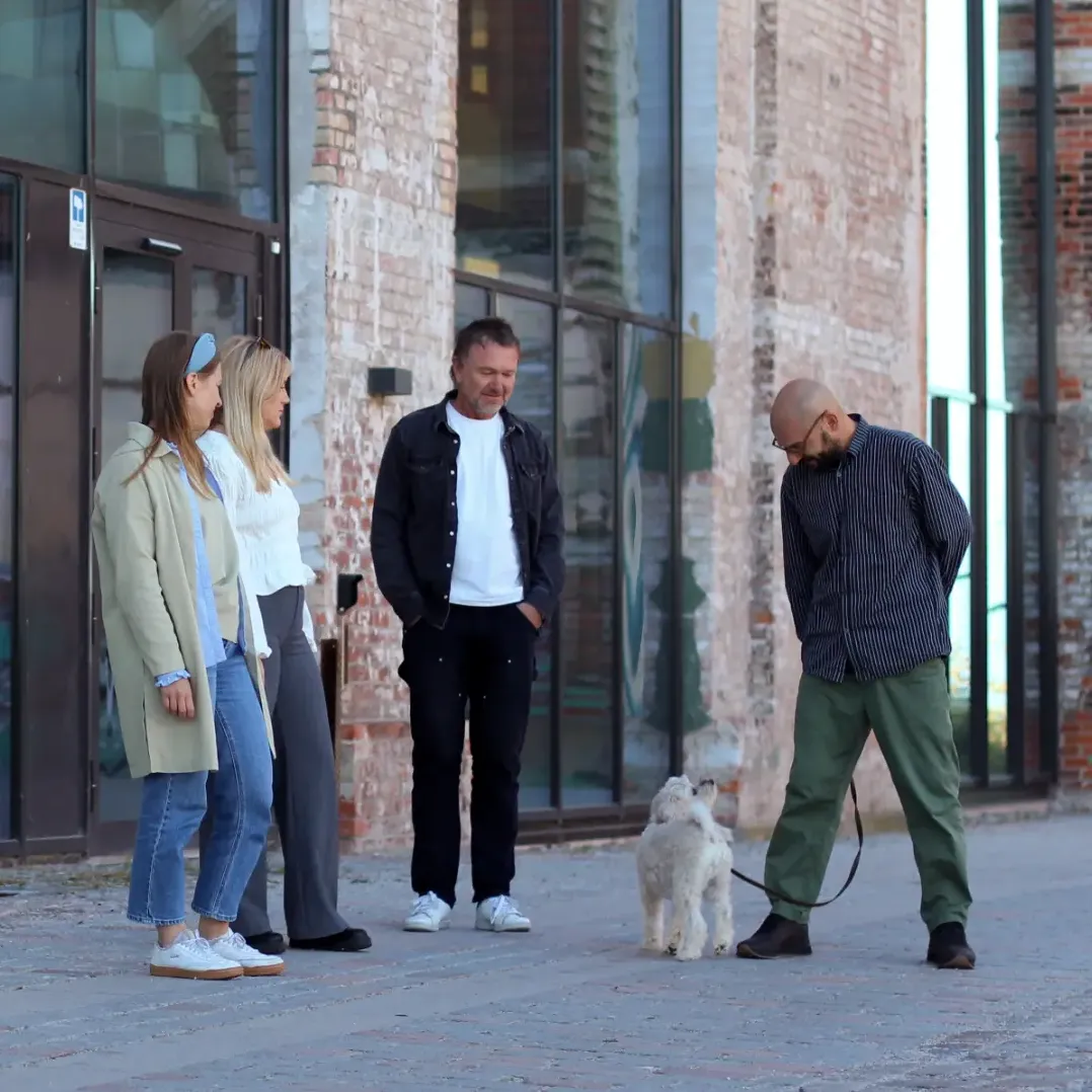 Människor som står utanför en byggnad med en hund i koppel, för en avslappnad konversation i centrum.