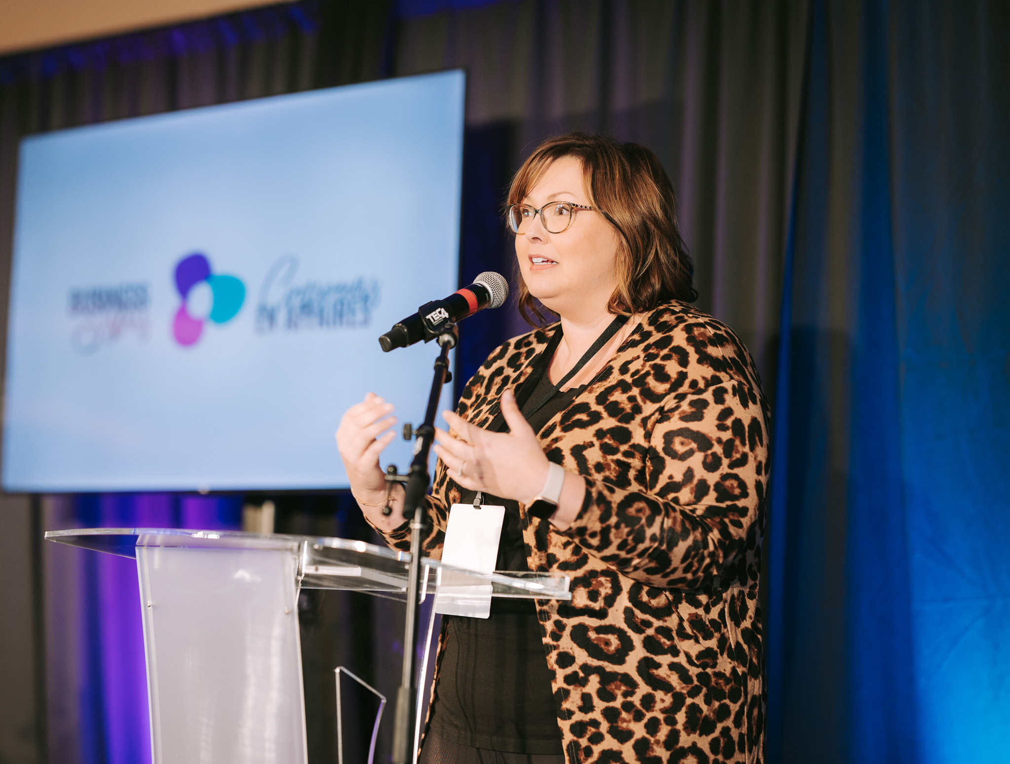 Chantal Lavergne wearing a leopard print jacket speaking at a podium with microphone at an event.