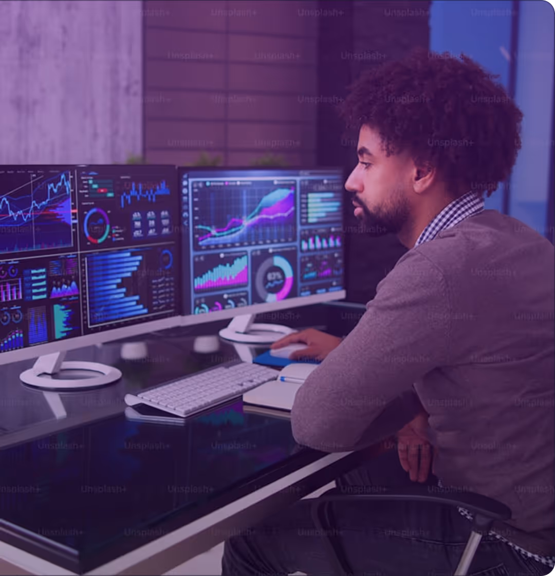 Man sitting at a desk analyzing data charts on two large computer monitors.