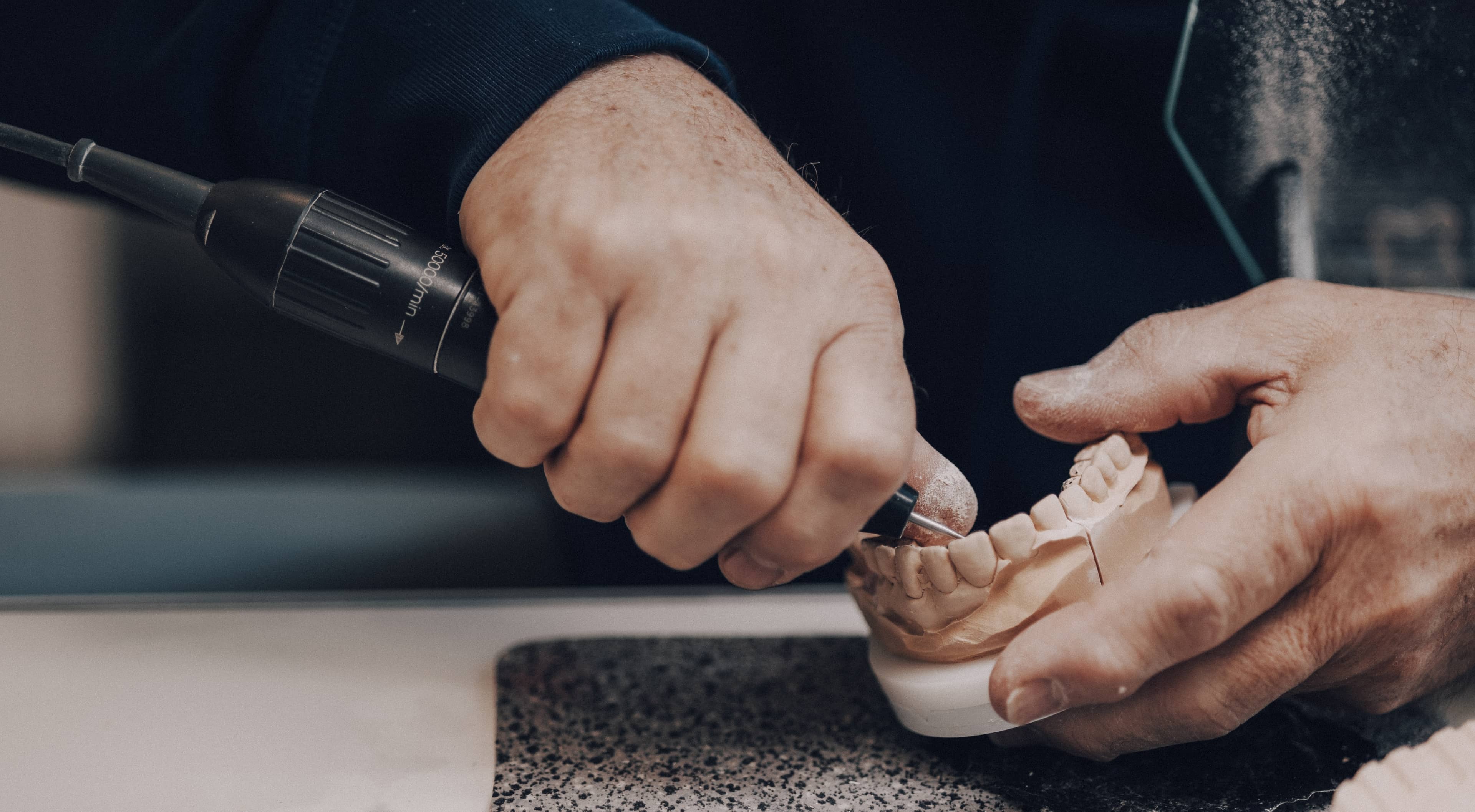 Zahntechniker schleift Zahnersatz mit Winkelstück am Gipsmodell – präzise Okklusion Höhn Dentaltechnik