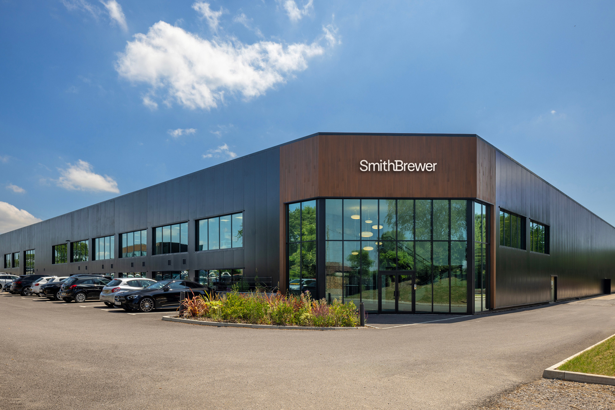 Modern office building with large glass windows and the name SmithBrewer on the facade under a blue sky.
