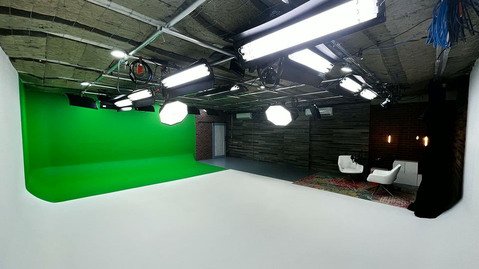 Studio A green screen and white cyc, with a lounge set of white chairs at the back of the stage.