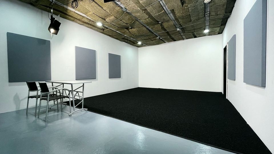 Wide view of Studio B with white walls, grey wall panels, a black carpet floor and a table with chairs.
