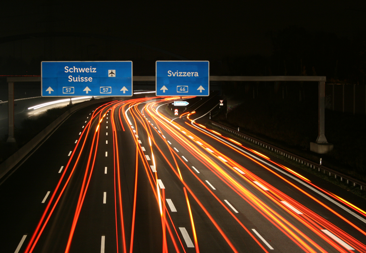 Motorway at night with light trails and border signs reading Schweiz, Suisse, Svizzera