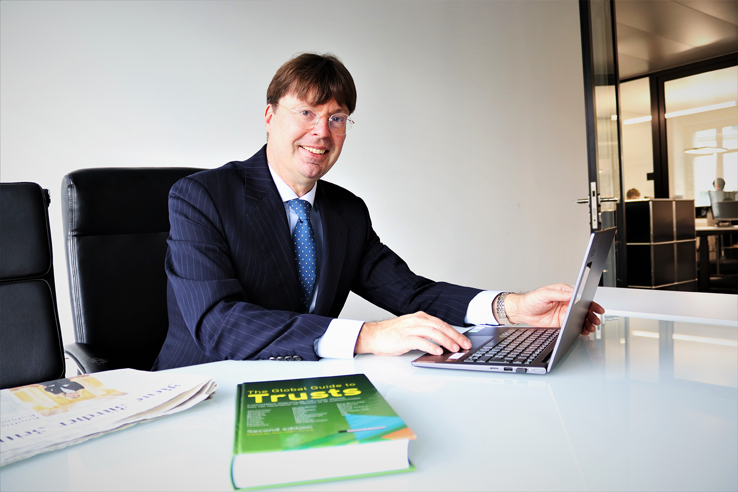 Man in a suit working at a laptop with a book on trusts on the desk