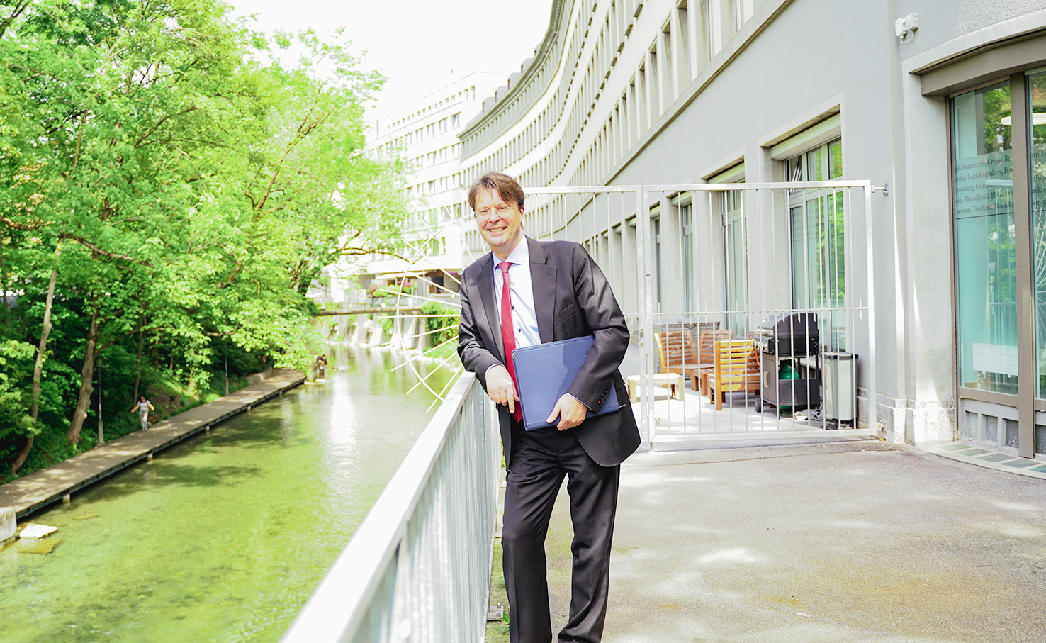 Man in a suit holding a folder on a footbridge over a city canal