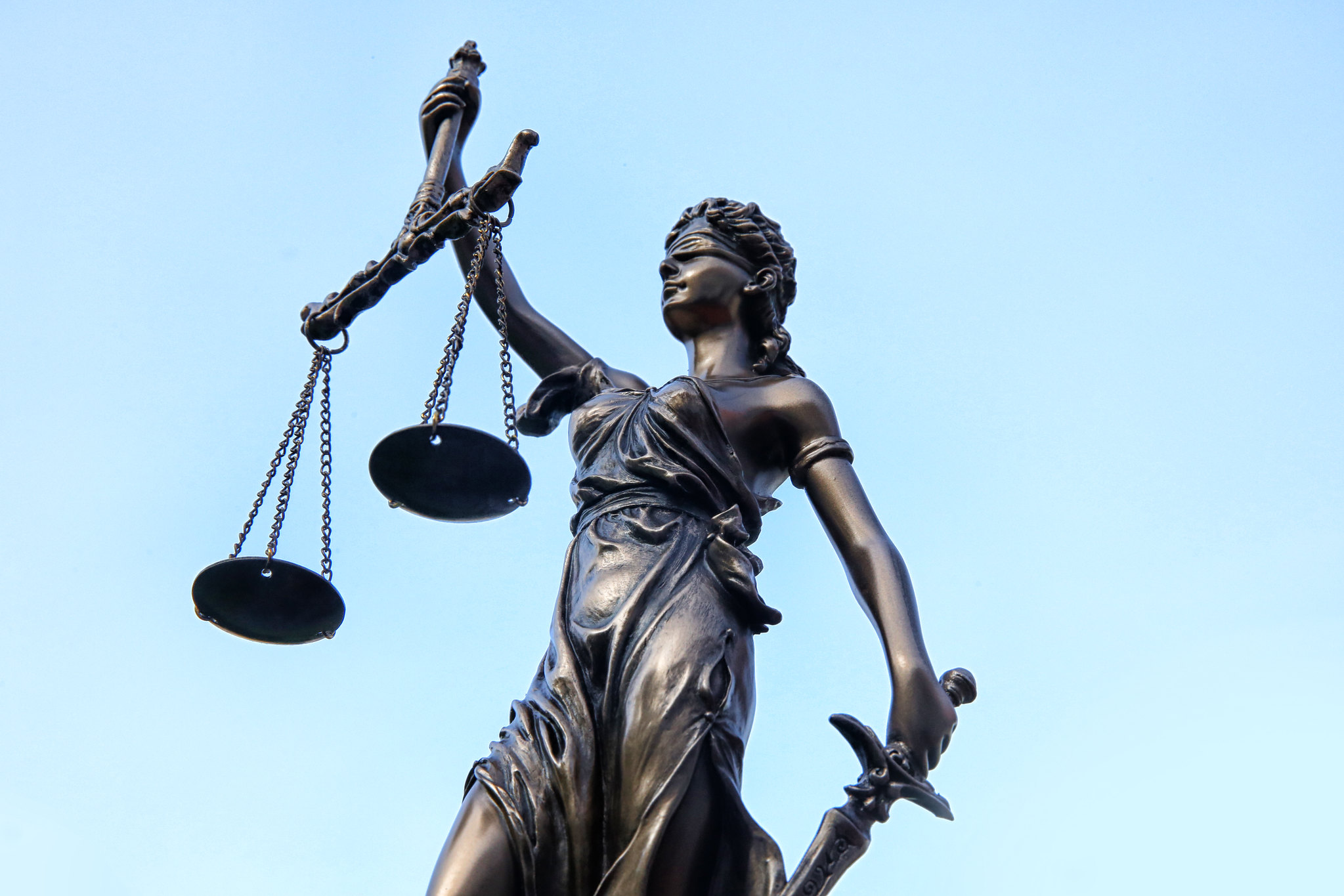 Bronze statue of Lady Justice holding scales against a blue sky