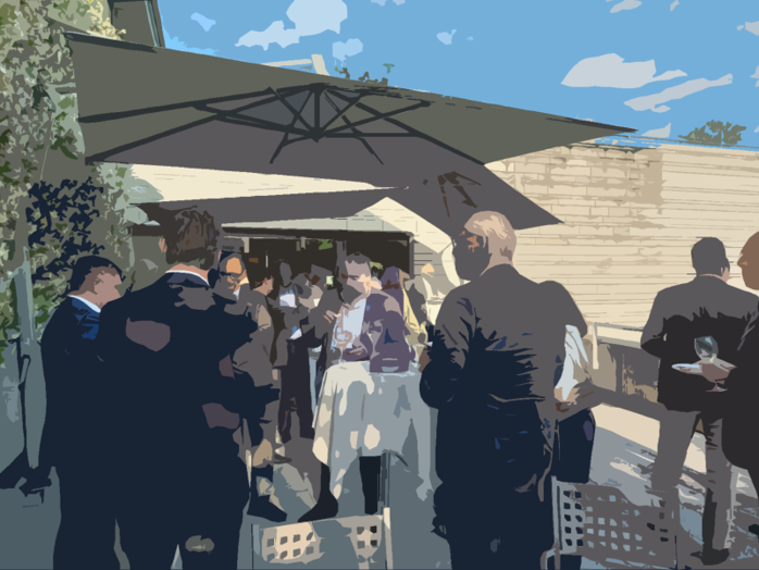 Guests in dark suits at an outdoor reception under a large parasol