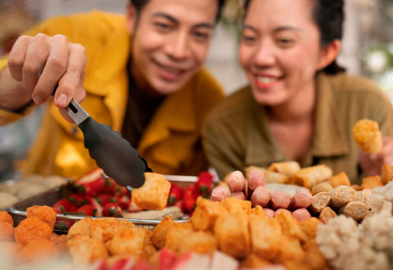 A young couple looking excited in front of a spread of food.