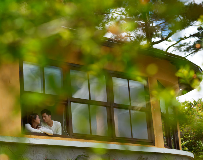 a pair of young asian couple sitting by the window of their eco-friendly hotel room overlooking the greenery around the hotel.t