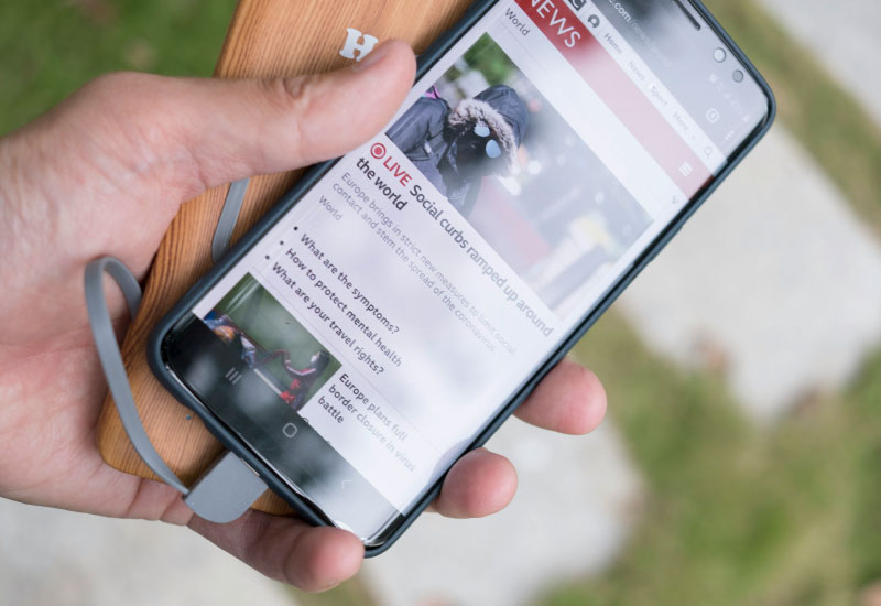 Person Holding Black Samsung Android Smartphone, with the screen displaying World News about social curbs ramped up around the world.