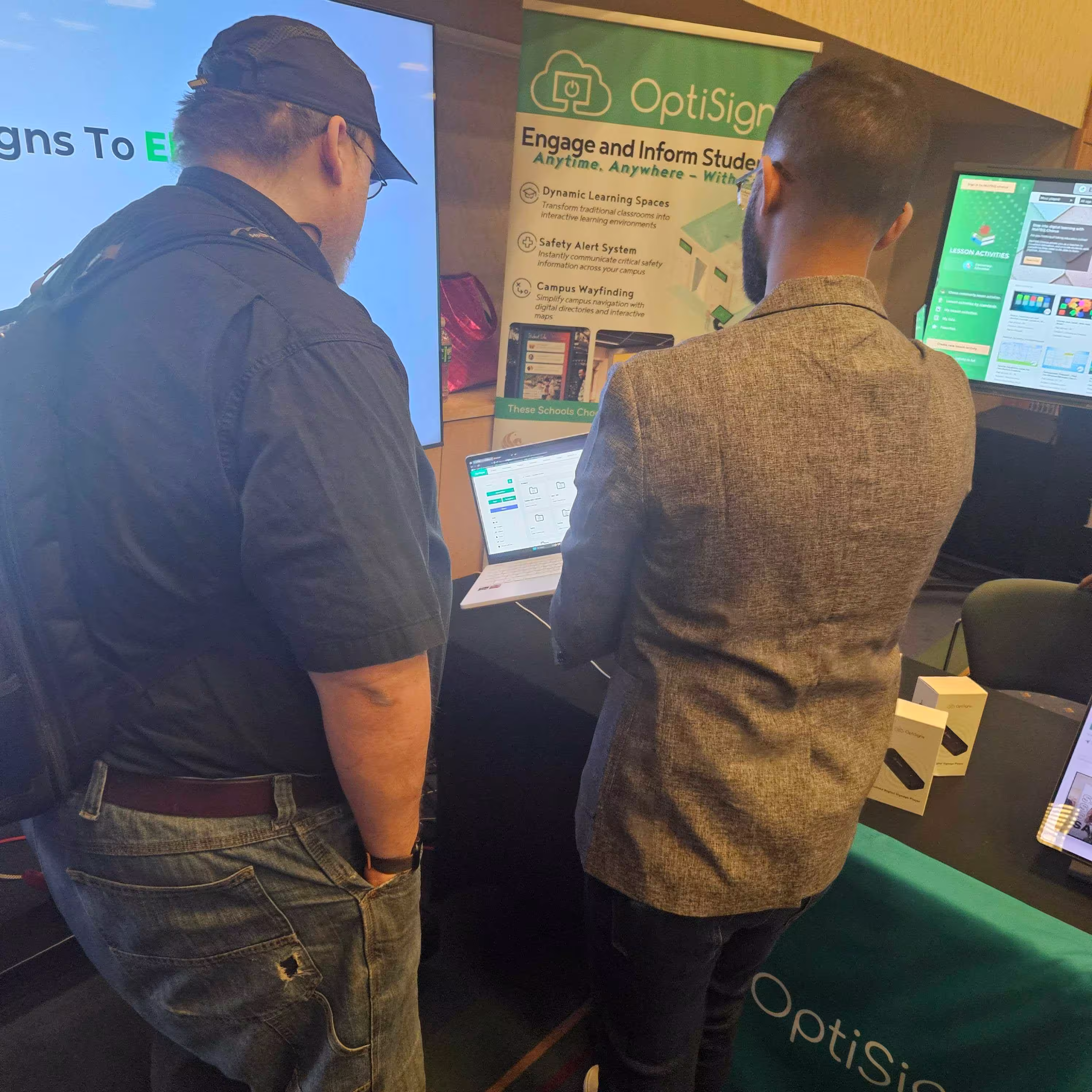 OptiSigns representative showcasing the OptiSigns platform on a laptop to a person on his left.
