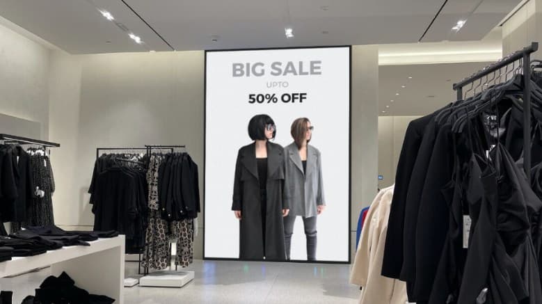 Dynamic signage on the wall inside a retail showroom with women's apparel, promoting a discount on the products.
