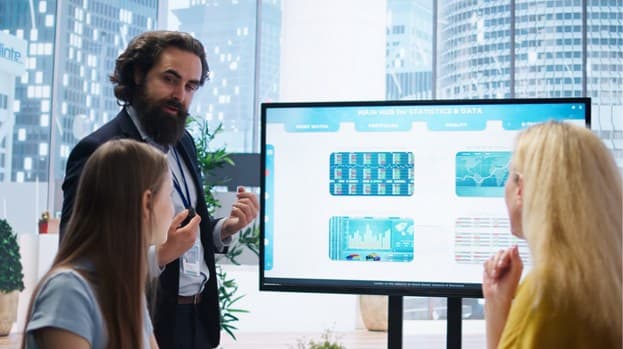 Employees in an office gathered around a digital signage screen with company information.