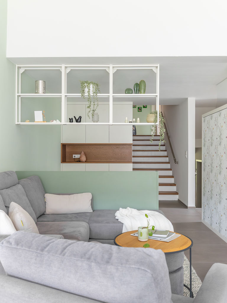 Graues Ecksofa mit einer mintgrünen halbhohen Raumteilerwand und einem weißen Raumteilerregal im Hintergrund.