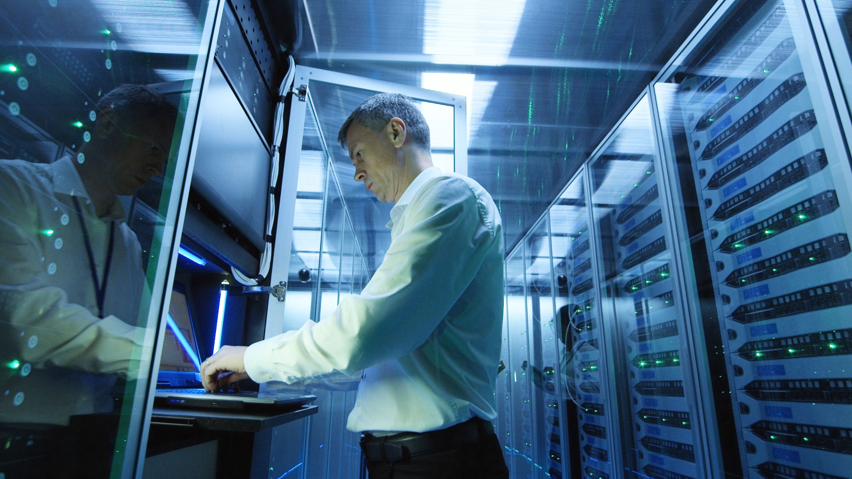 A man in a server room working on a laptop.