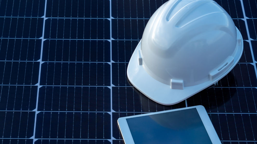 A hard hat and tablet on a solar panel.