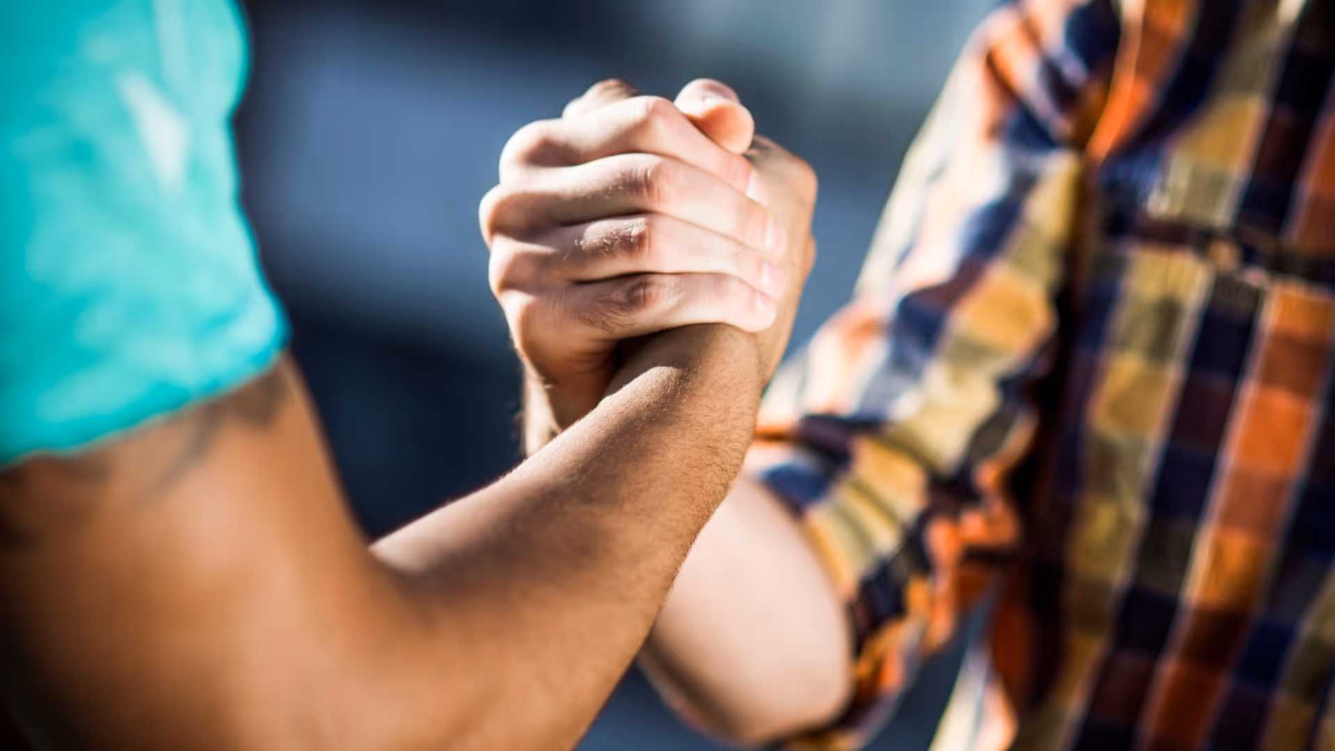 Close-up of two people clasping hands in a handshake or arm-wrestling grip.