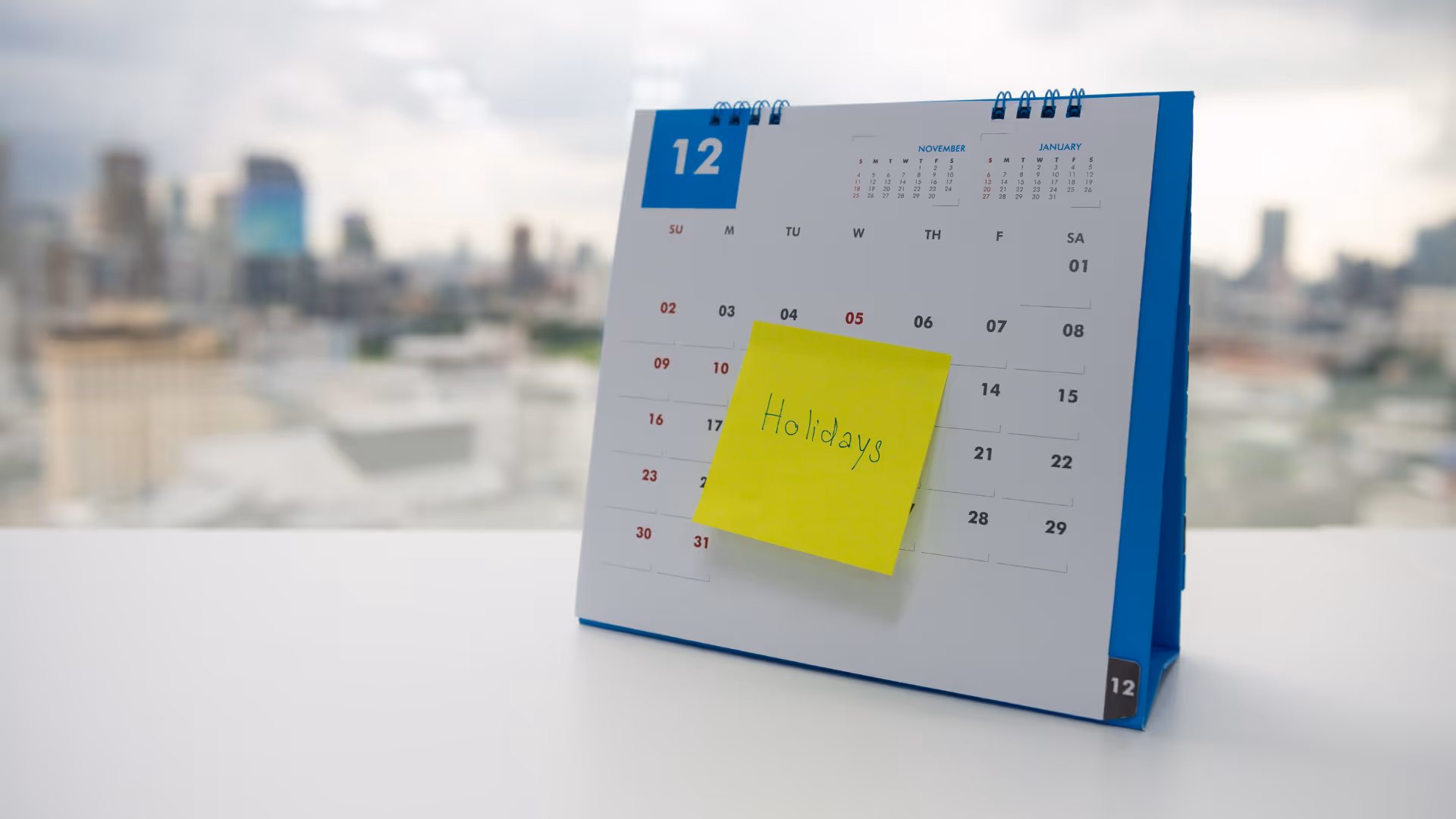 Desk calendar open to December with a yellow sticky note that says Holidays.