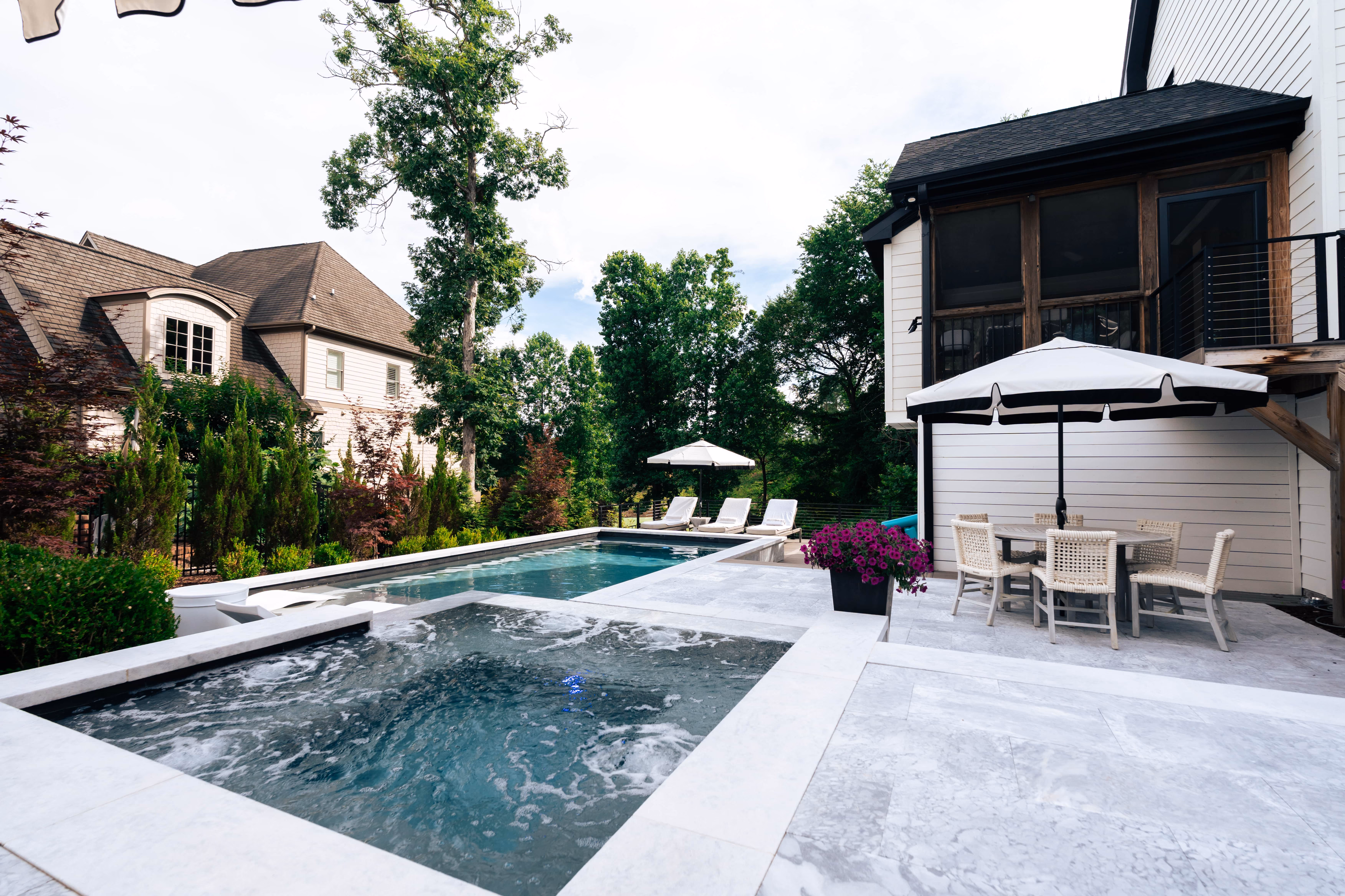 A luxury custom pool build and modern patio design featuring lounge chairs next to a private swimming pool in Raleigh, NC.
