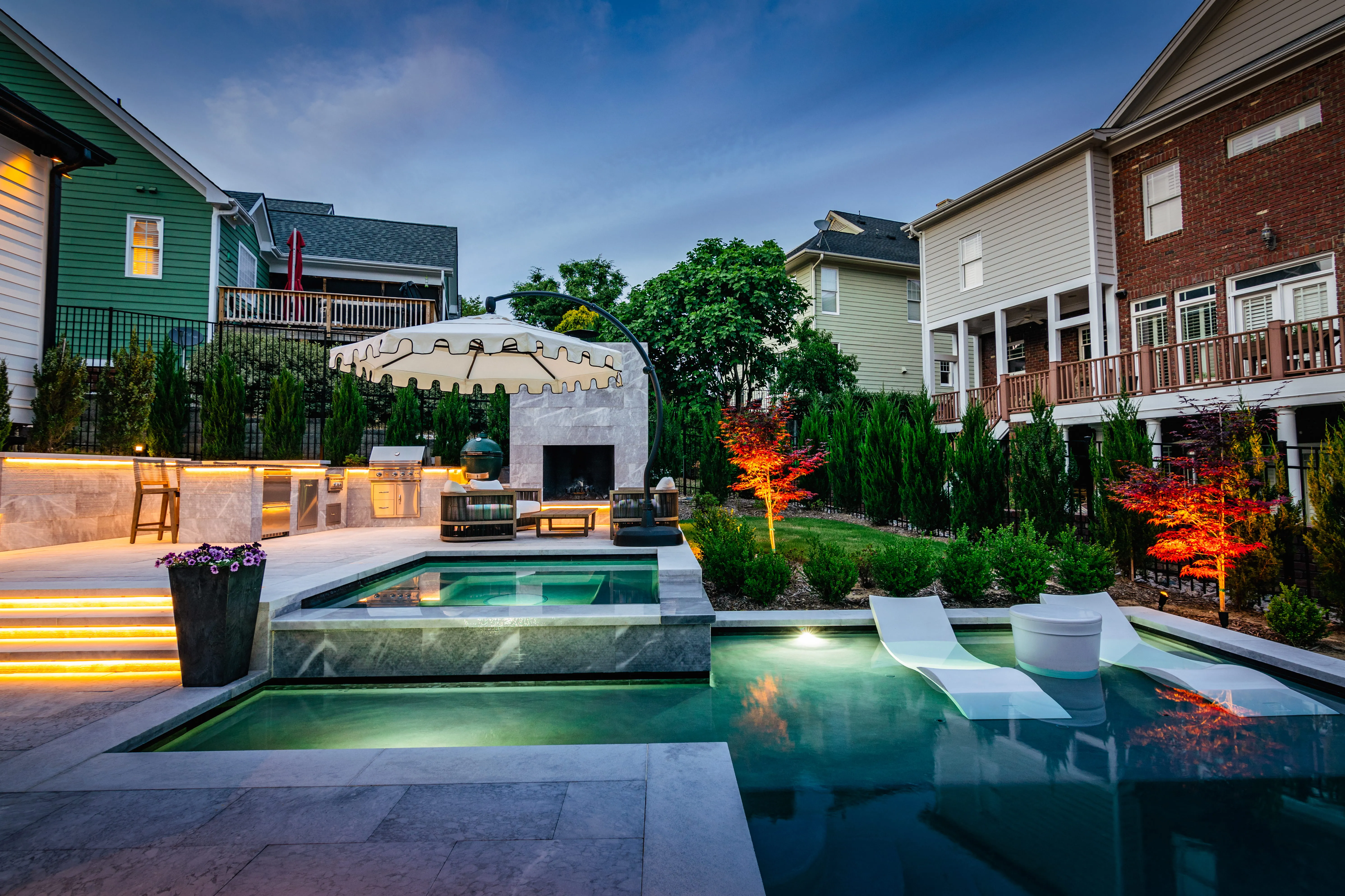 Custom luxury backyard design featuring a multi-level swimming pool, a built-in outdoor kitchen island, and glass fencing in Raleigh, NC by Currin Outdoor Living.