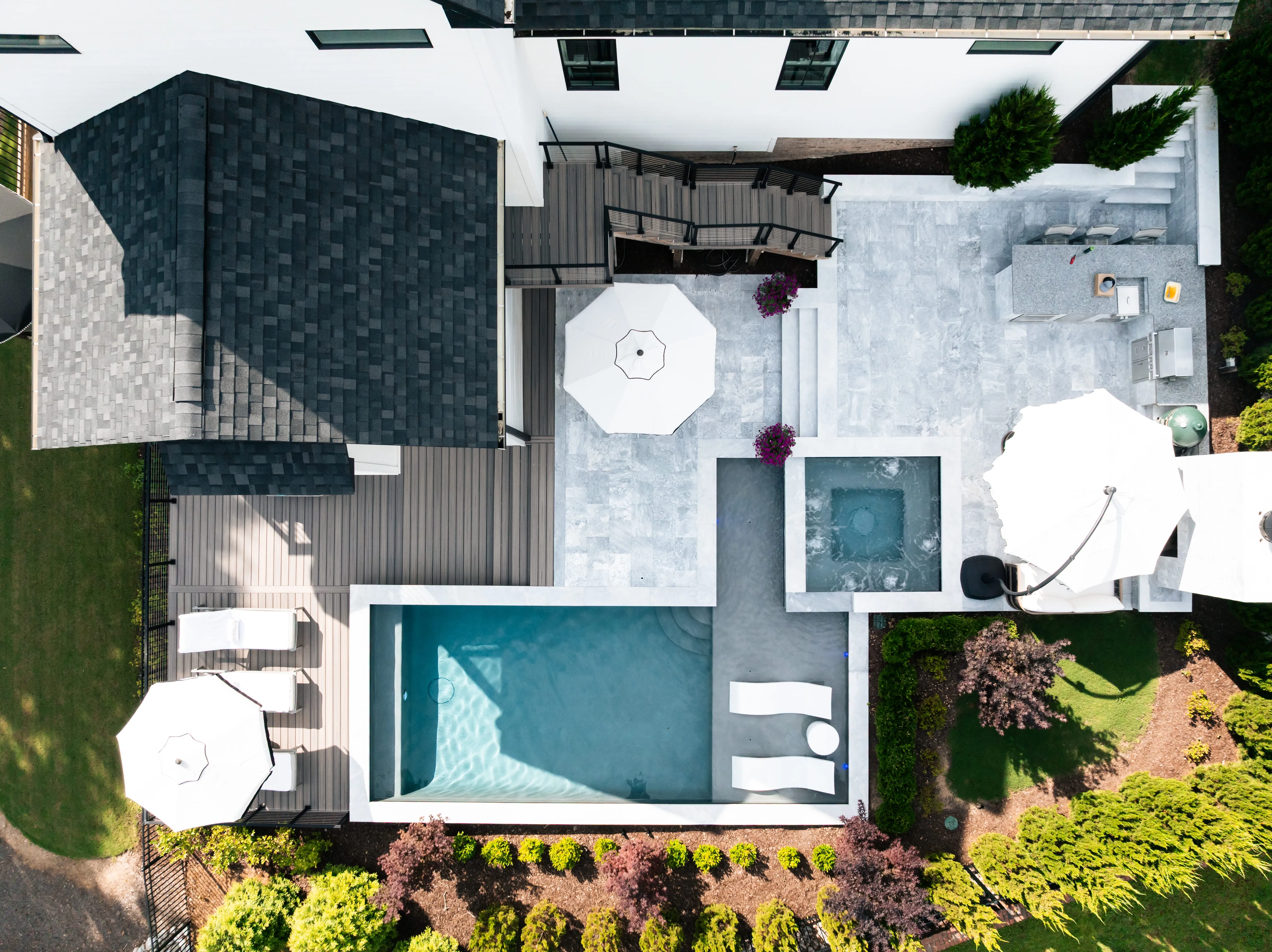 An aerial perspective of a premium residential backyard transformation in Raleigh, NC, featuring a custom inground swimming pool, stone patio lounge, and elegant landscaping design by Currin Outdoor Living.