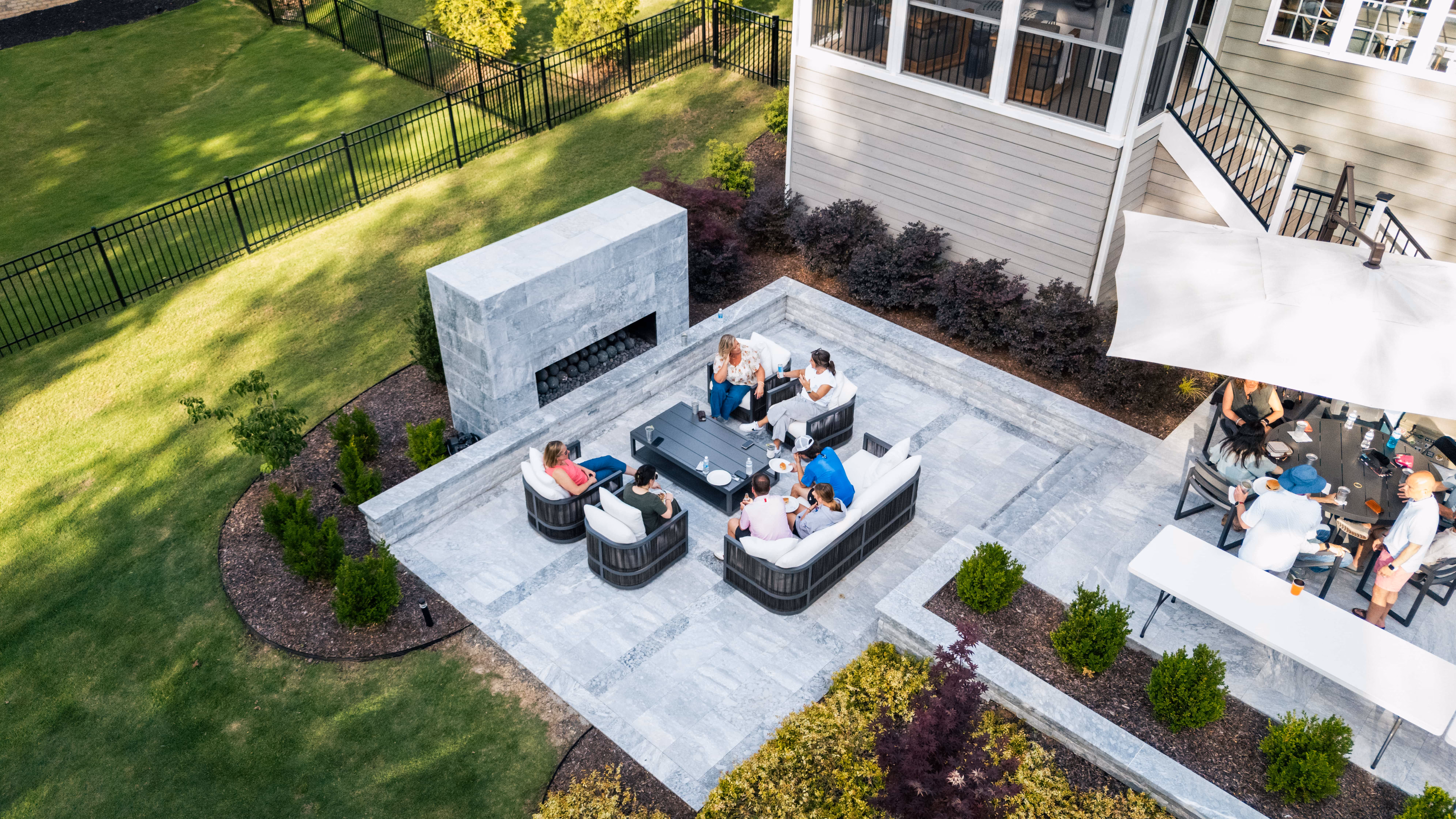 An aerial view of a custom-designed luxury backyard in Raleigh, NC, by Currin Outdoor Living, featuring an inground swimming pool, modern stone patio lounge, and professional landscape installation.