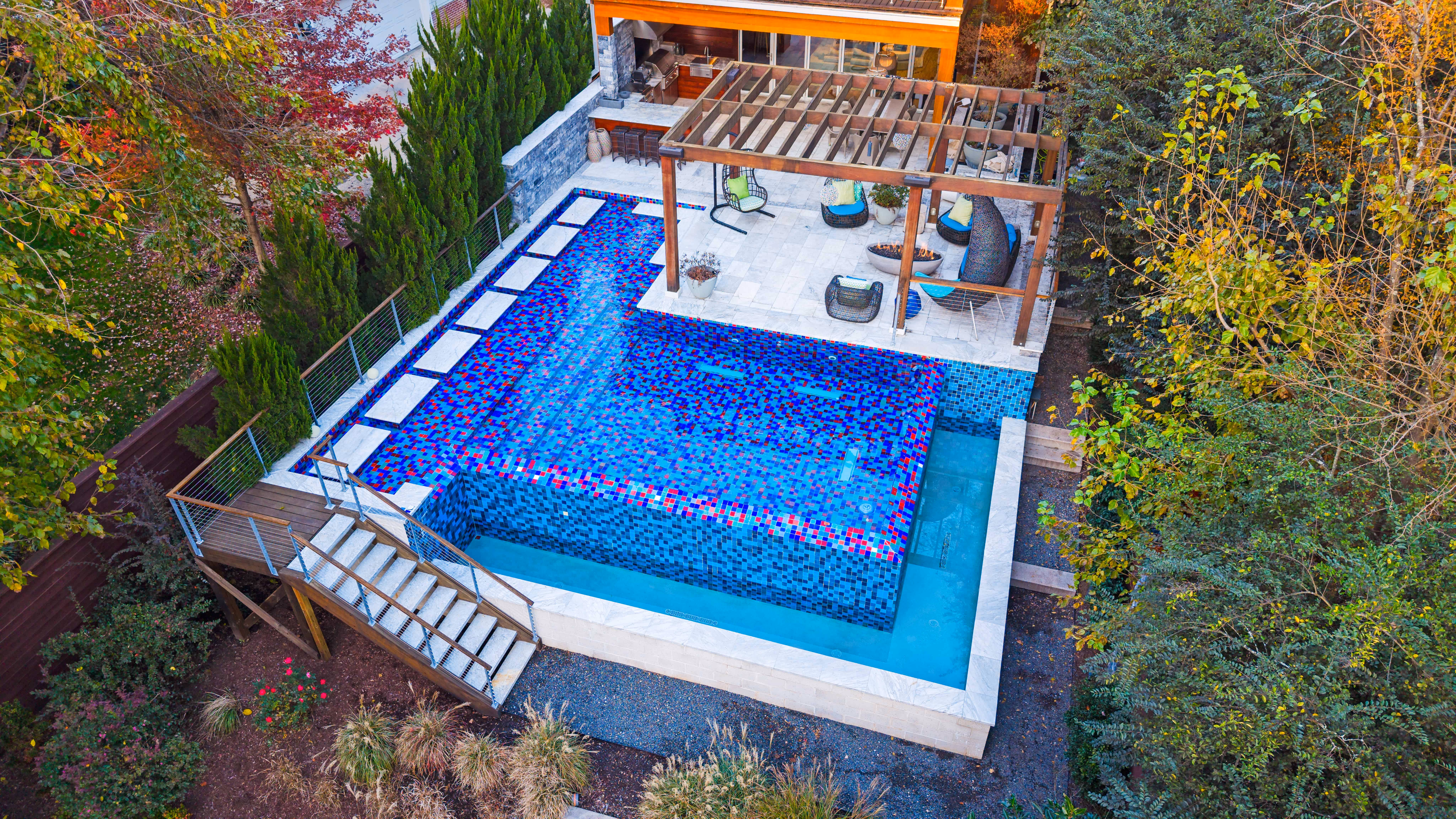 An aerial perspective of a premium residential backyard transformation in Raleigh, NC, featuring a custom inground swimming pool, stone patio lounge, and elegant landscaping design by Currin Outdoor Living.