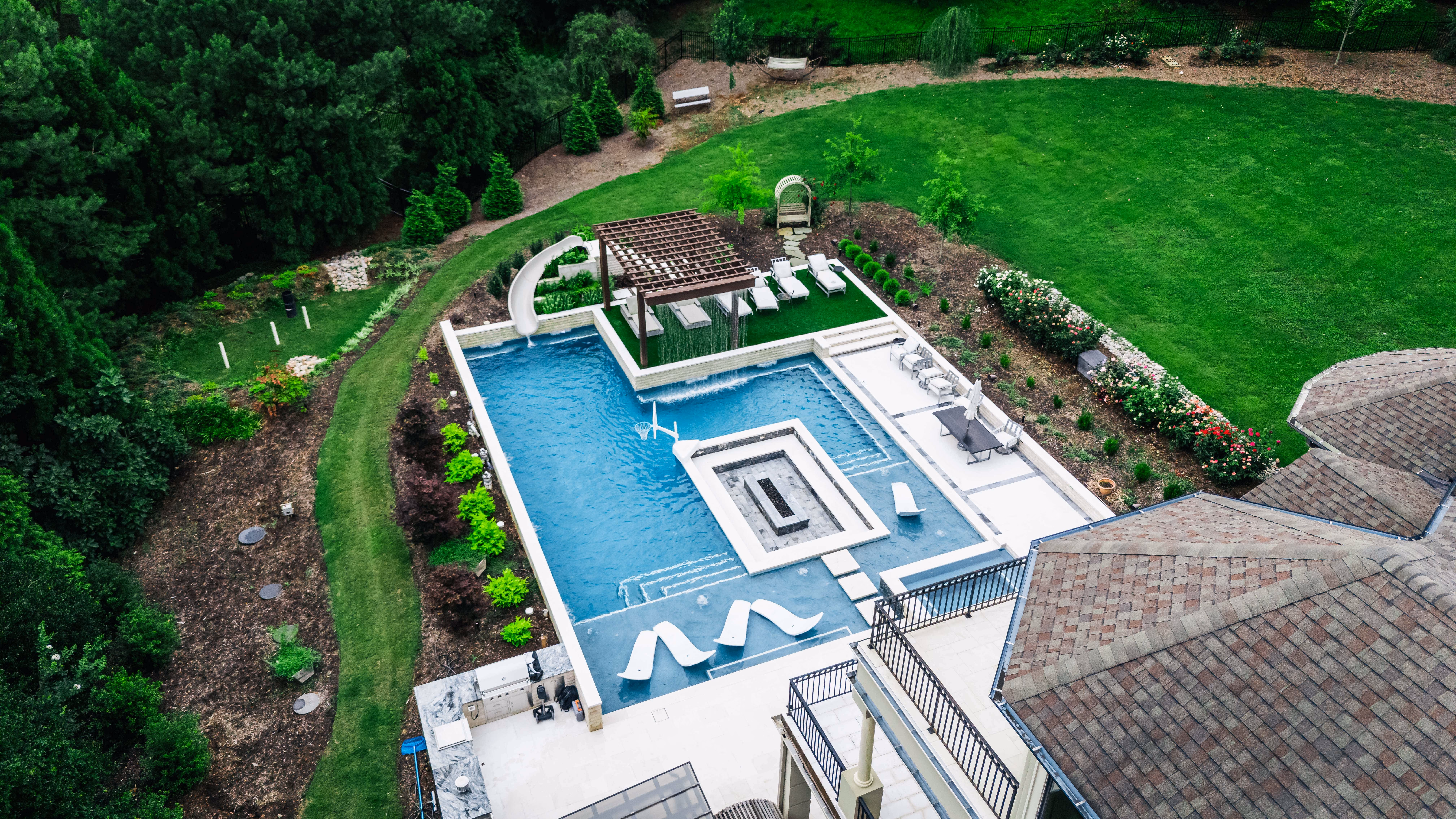 An aerial perspective of a premium residential backyard transformation in Raleigh, NC, featuring a custom inground swimming pool, stone patio lounge, and elegant landscaping design by Currin Outdoor Living.