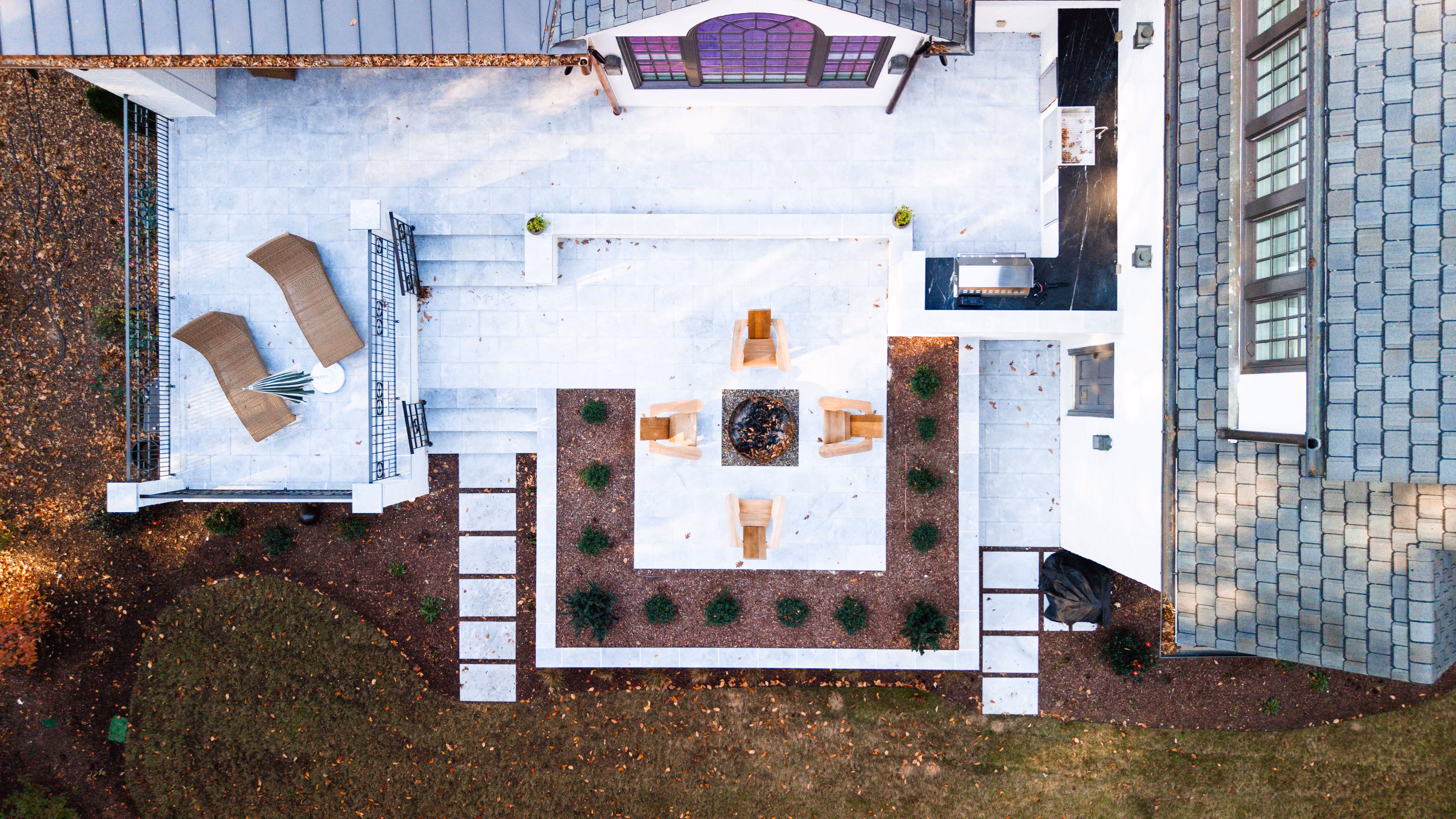 An aerial night view of a premier luxury backyard retreat in Raleigh, NC, designed by Currin Outdoor Living, featuring an illuminated inground swimming pool, modern patio lounge, and professional landscape lighting.