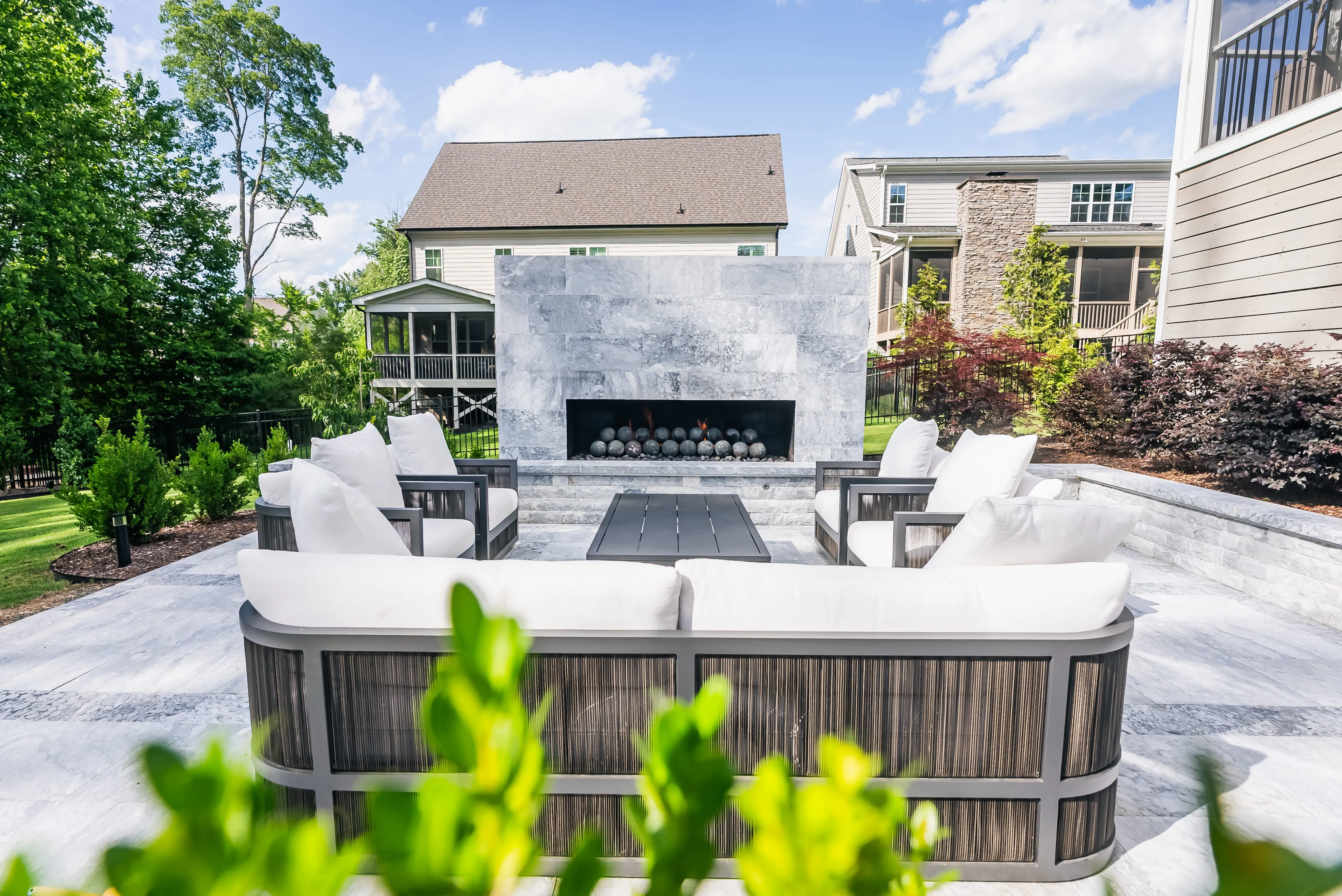 A cozy and modern outdoor lounge space designed by Currin Outdoor Living, featuring a sleek stone fire feature, premium patio furniture, and professional hardscaping in a private Raleigh, NC backyard.