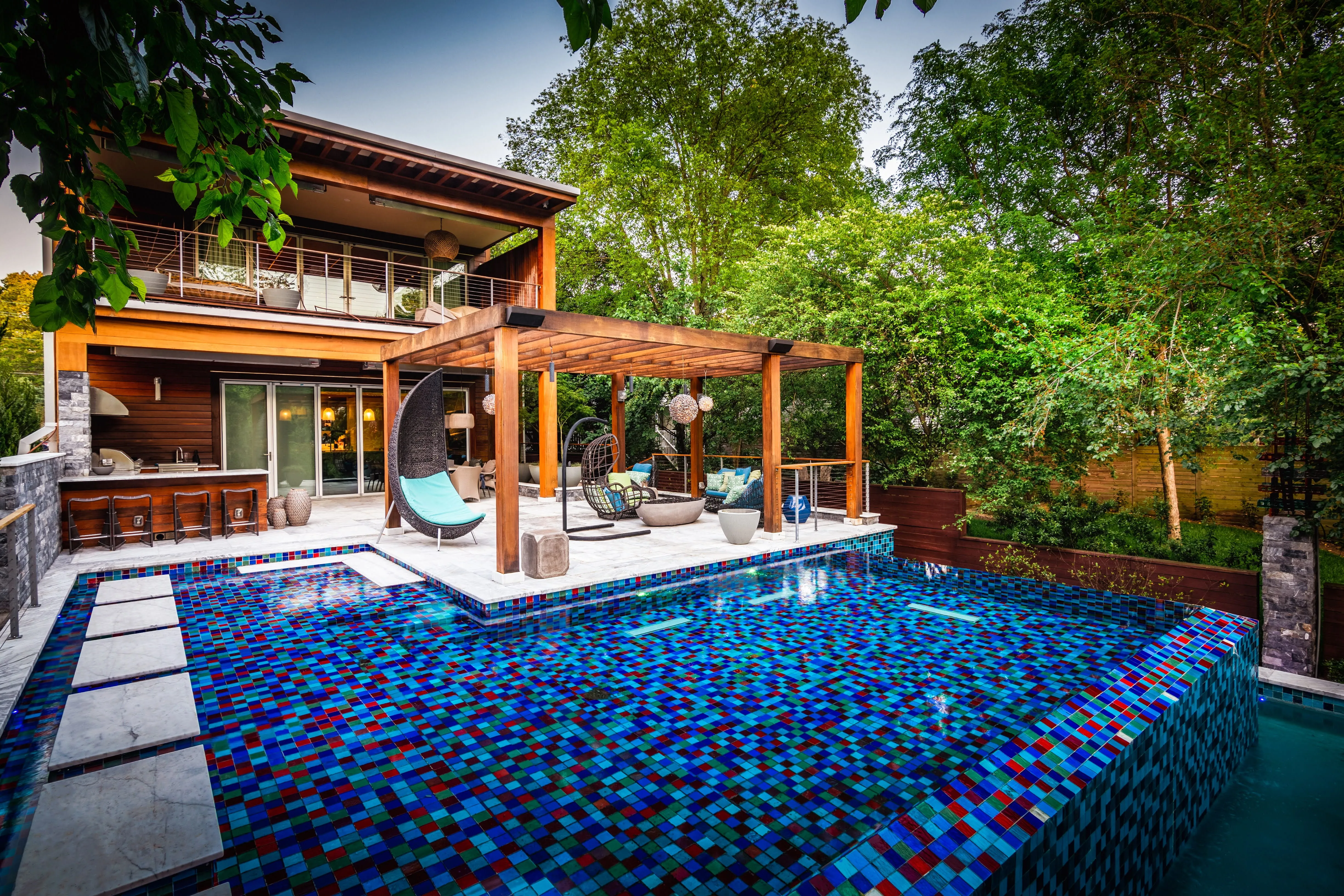 A breathtaking backyard oasis designed by Currin Outdoor Living, featuring a custom inground pool with modern water features, lush landscaping, and a spacious patio for resort-style outdoor entertaining in Raleigh, NC.