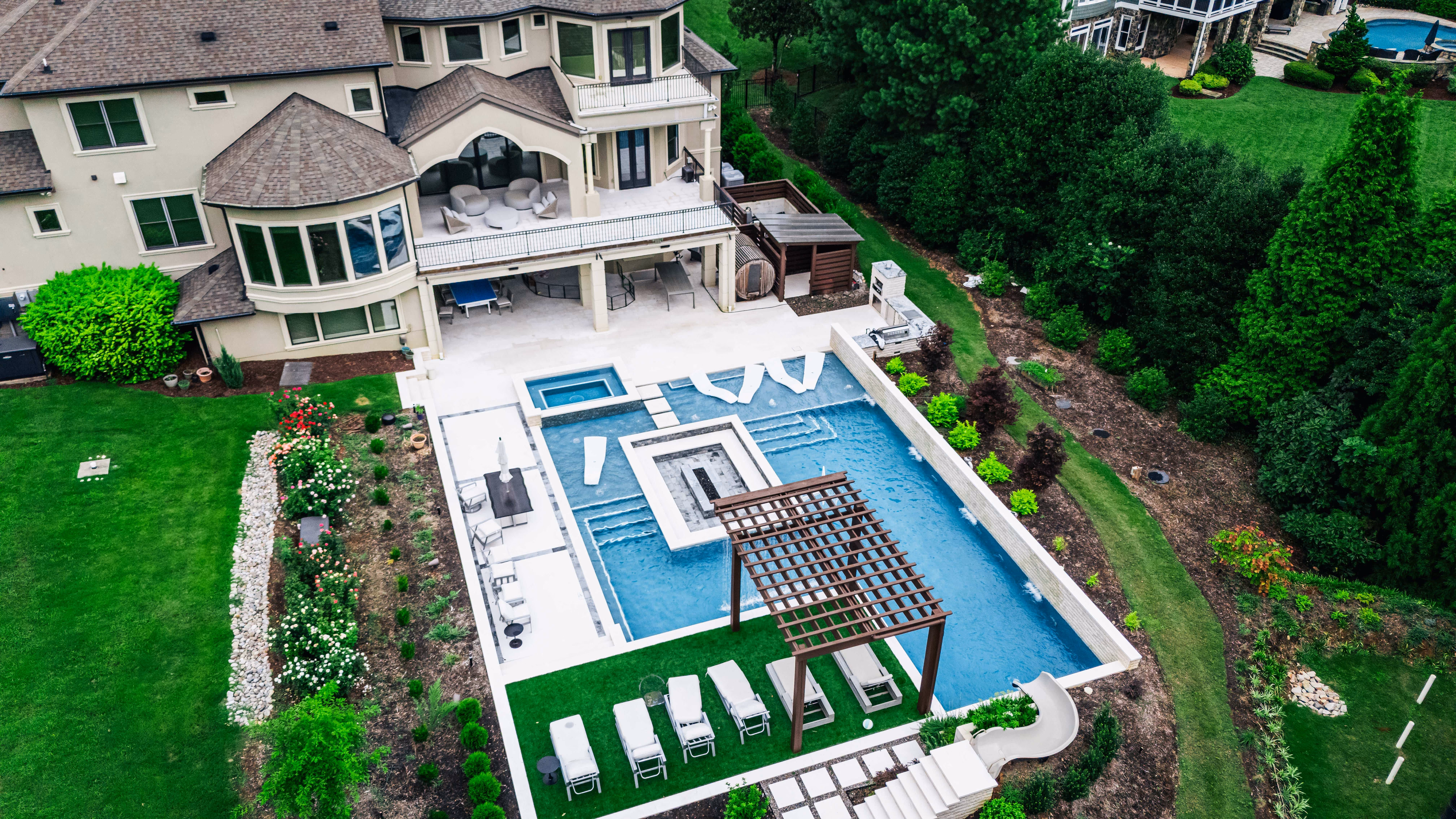 A high-end residential backyard featuring a custom inground swimming pool, integrated stone patio, and professional outdoor living design by Currin Outdoor Living in Raleigh, NC.