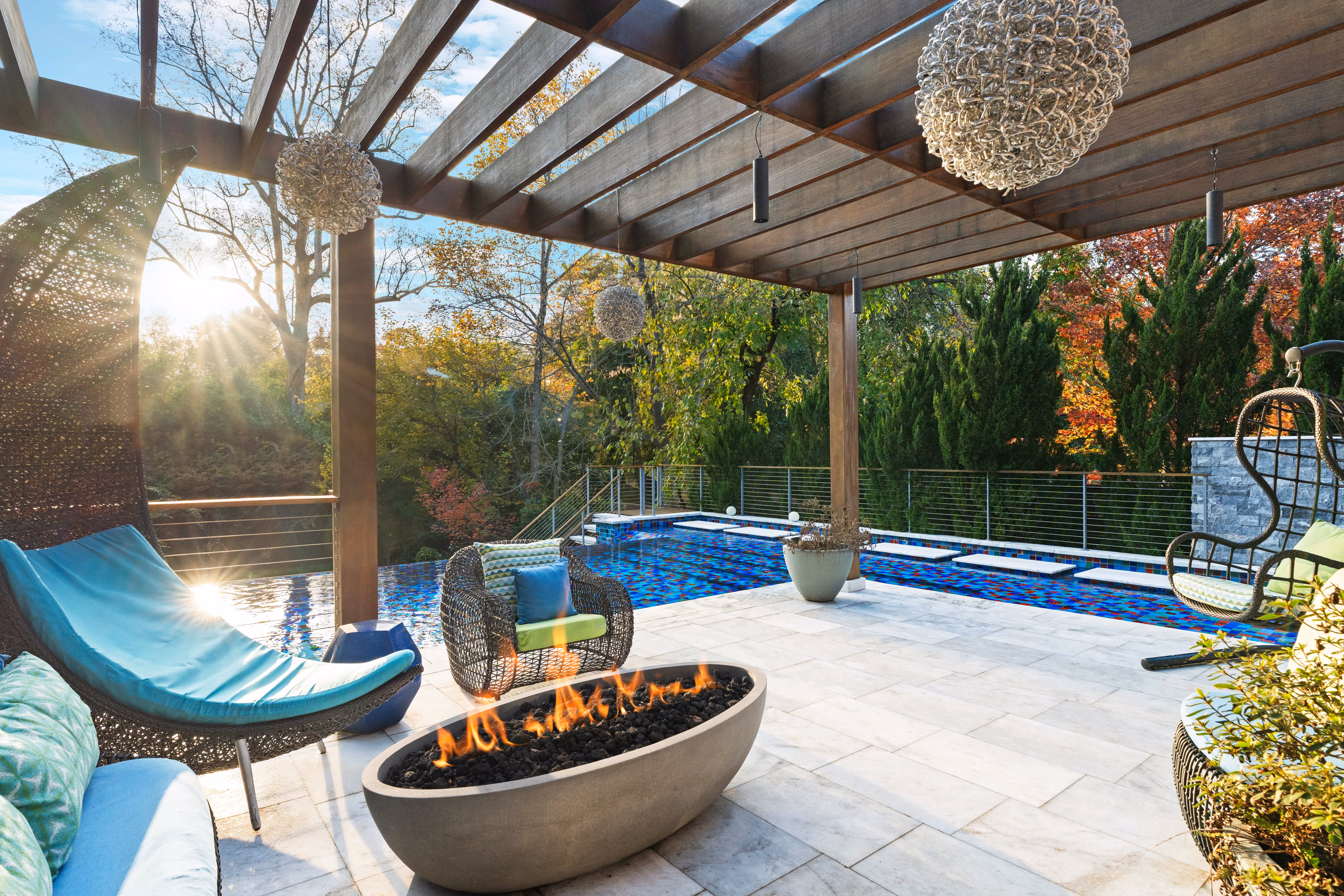 Ground-level view of a luxury backyard outdoor living space featuring a custom wooden modern pergola over a premium stone paver patio lounge next to an inground swimming pool built by an outdoor living company in Raleigh, NC.