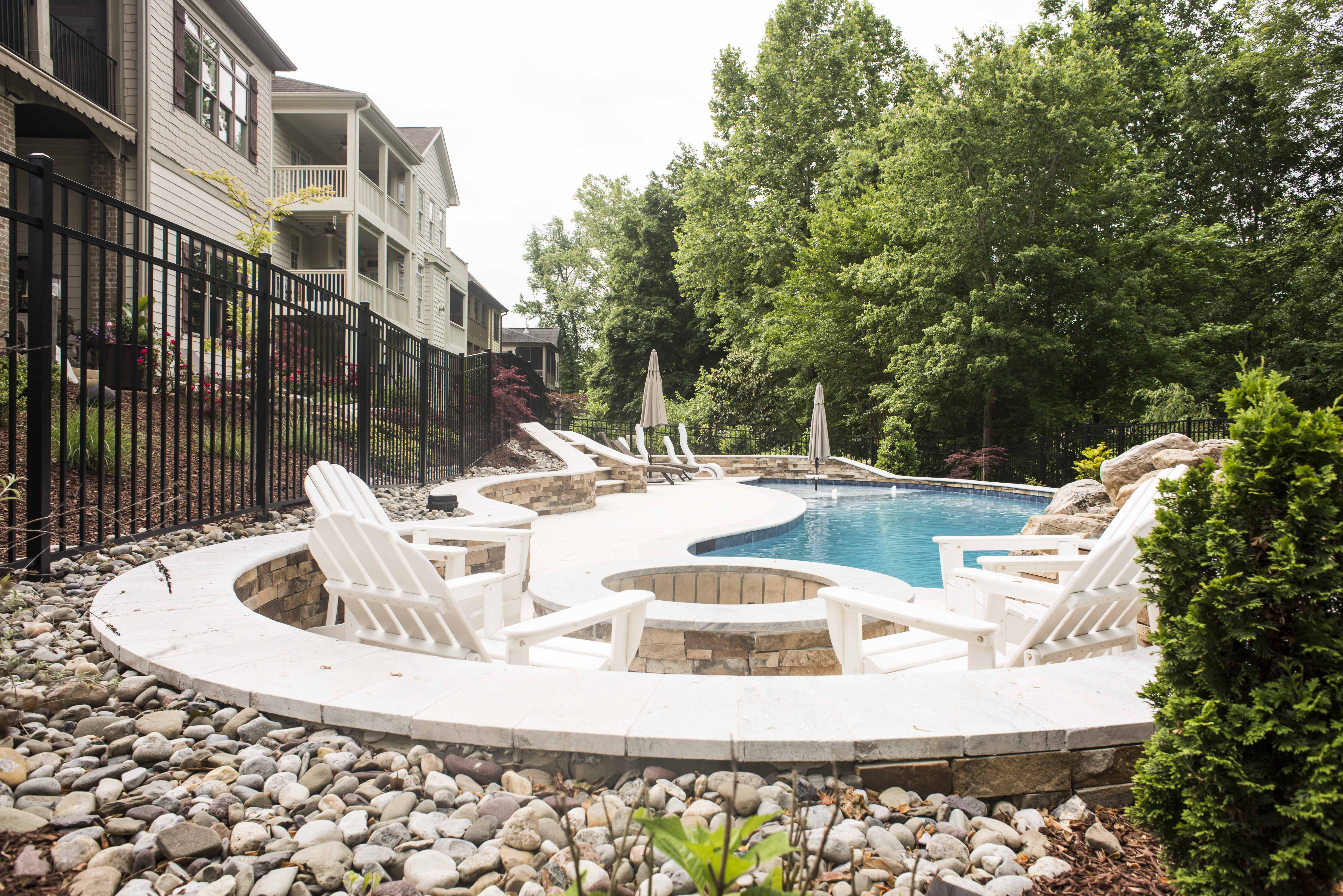 Custom-designed swimming pool with a natural stone rock waterfall, concrete pool deck, and elegant residential architecture backdrop built by a custom pool builder in Raleigh, NC.