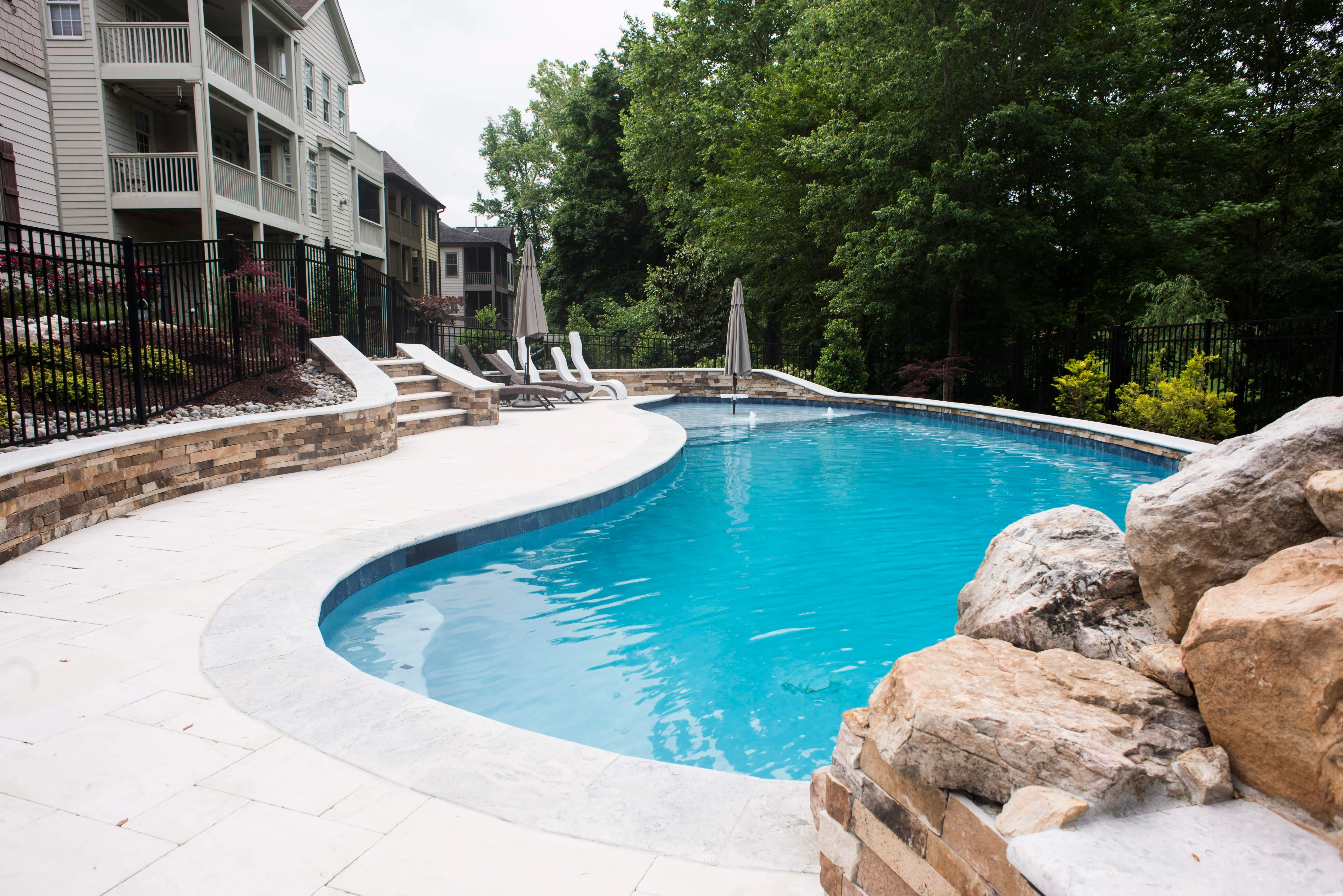 Custom lagoon swimming pool design featuring a natural stone rock waterfall, a smooth concrete pool deck, and lush backyard landscaping built by a pool builder in Raleigh, NC.