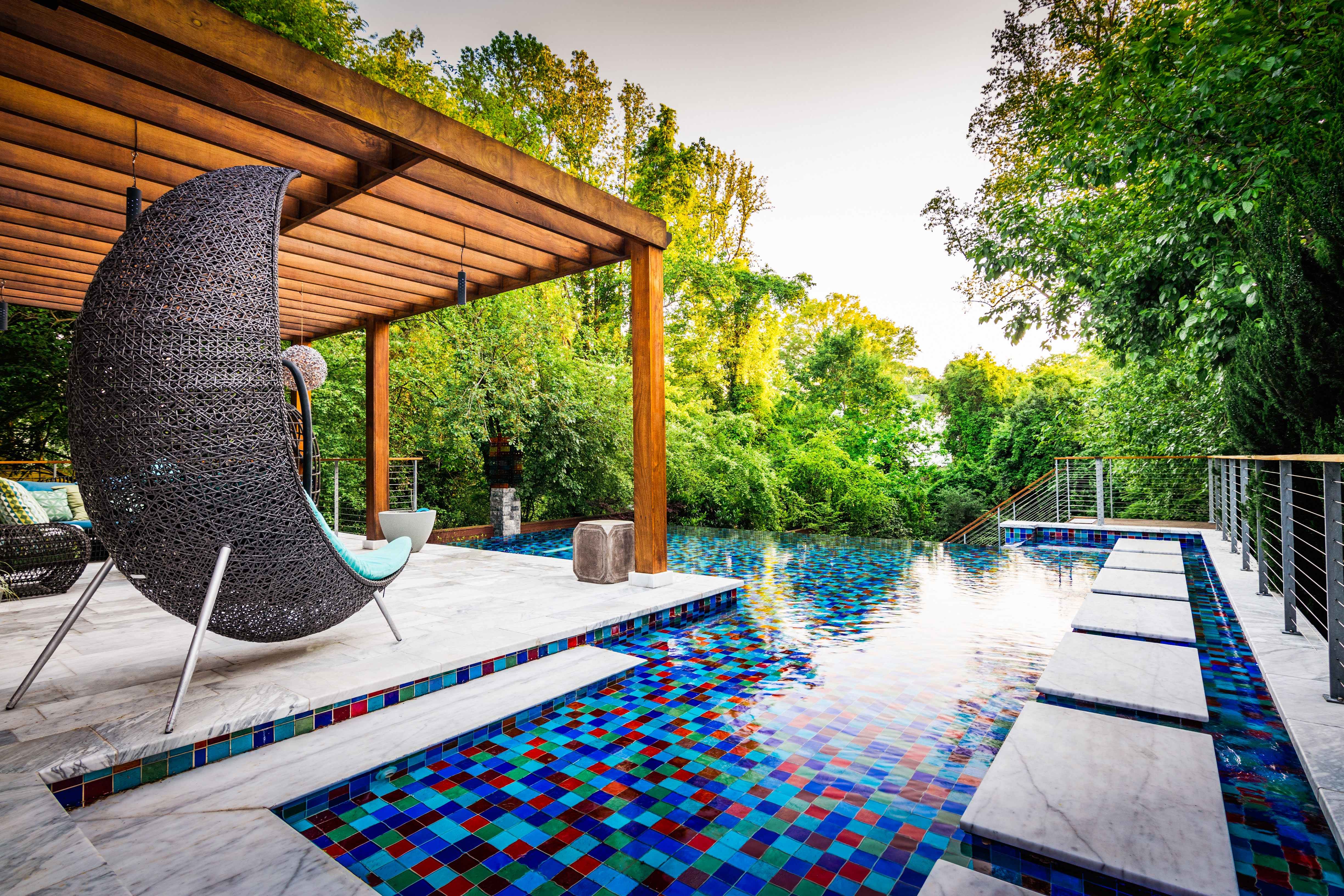 Luxury backyard pool design featuring a custom dark wood patio pergola, a unique woven hanging lounge chair, and premium landscaping built by a custom pool builder in Raleigh, NC.