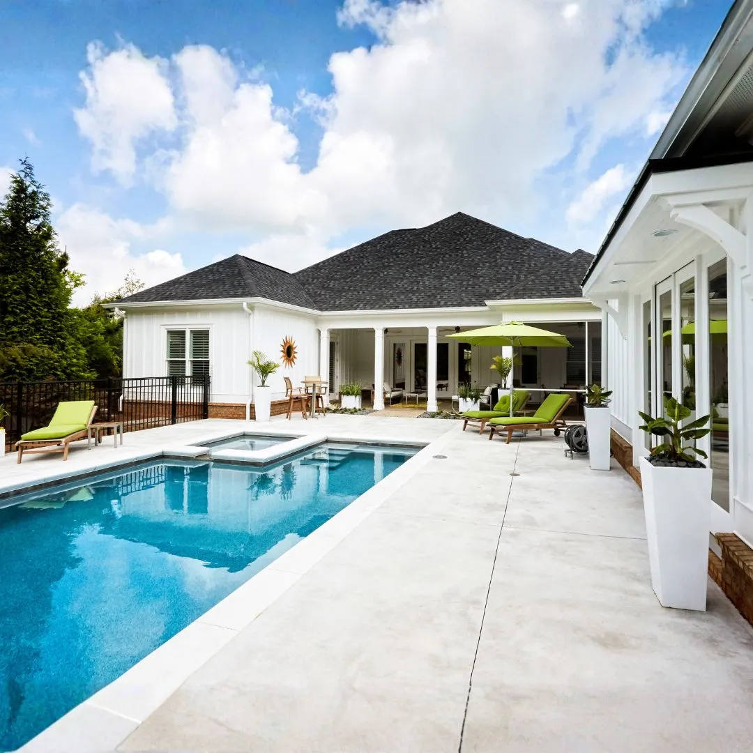 Custom rectangular inground swimming pool featuring clear blue water, light stone paver patio surround, and modern home exterior in Fuquay-Varina, NC.