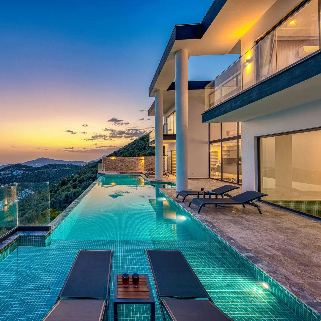 Custom illuminated inground infinity pool with ambient lighting and poolside lounge seating alongside a modern luxury home at sunset in Fuquay-Varina, NC.