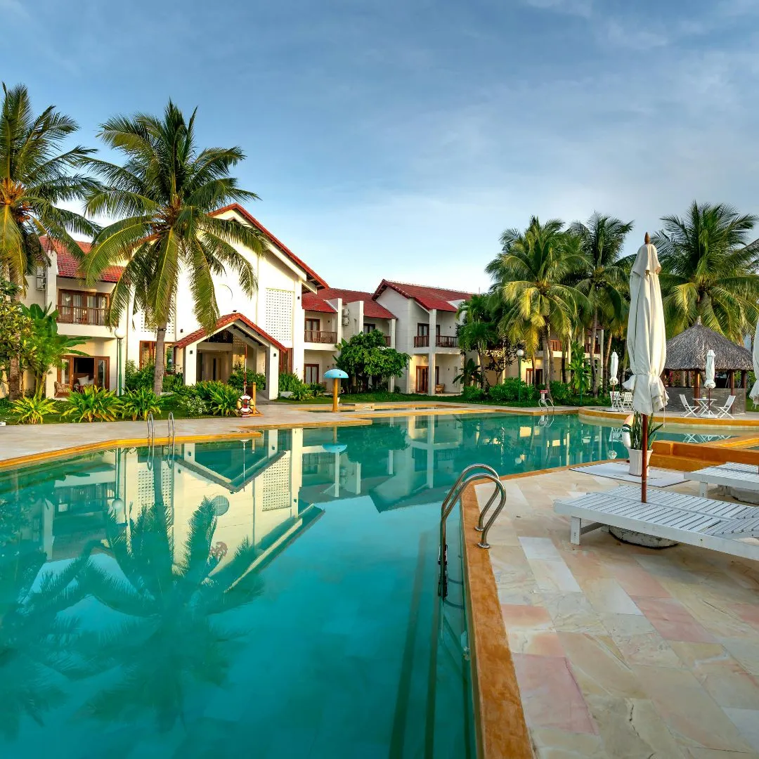 Custom resort-style inground swimming pool featuring clear turquoise water, light stone coping, patio lounge area, and tropical palm tree landscaping in Garner, NC.