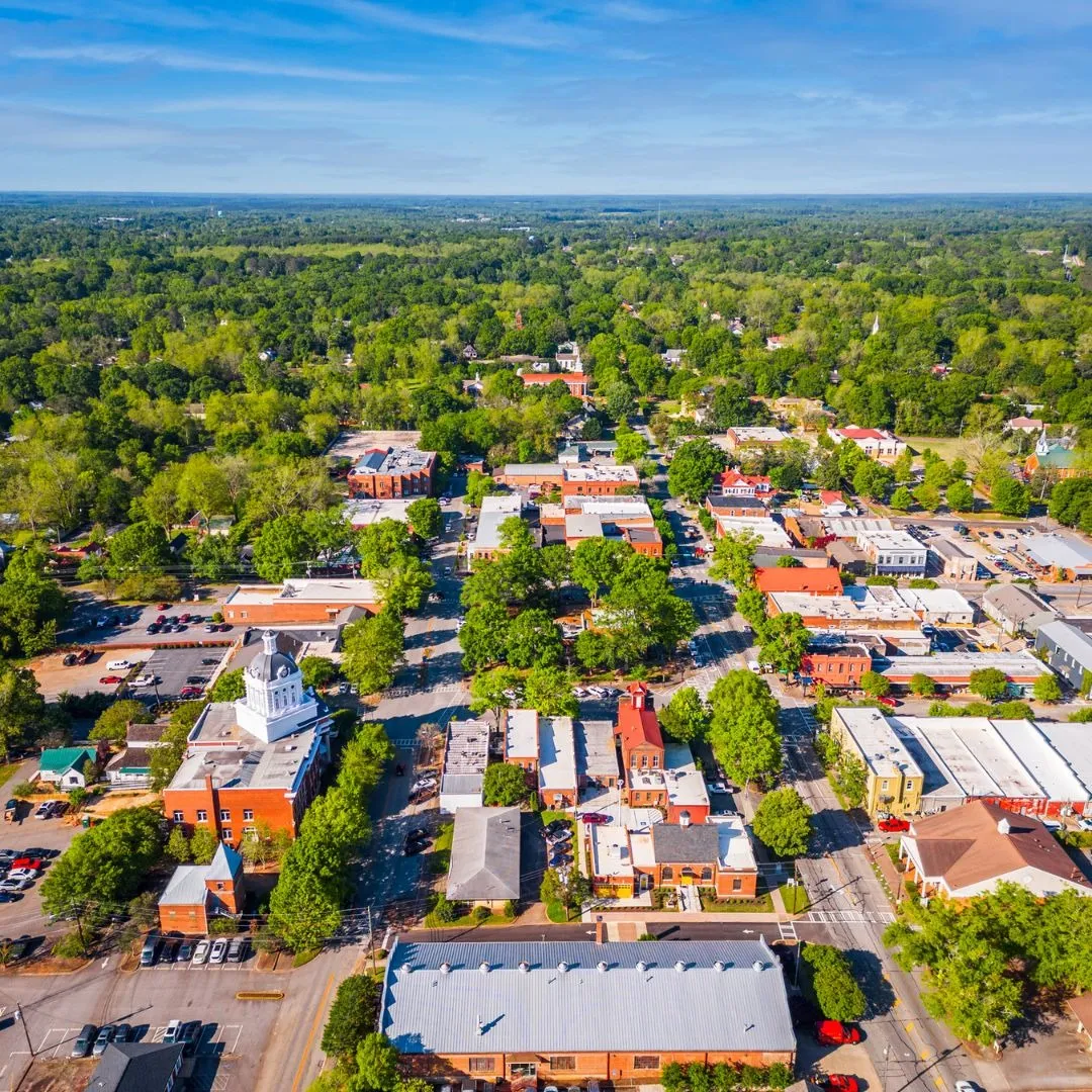 Aerial view of town center streets, buildings, and green canopy representing the Holly Springs, NC service area for Currin Outdoor Living.