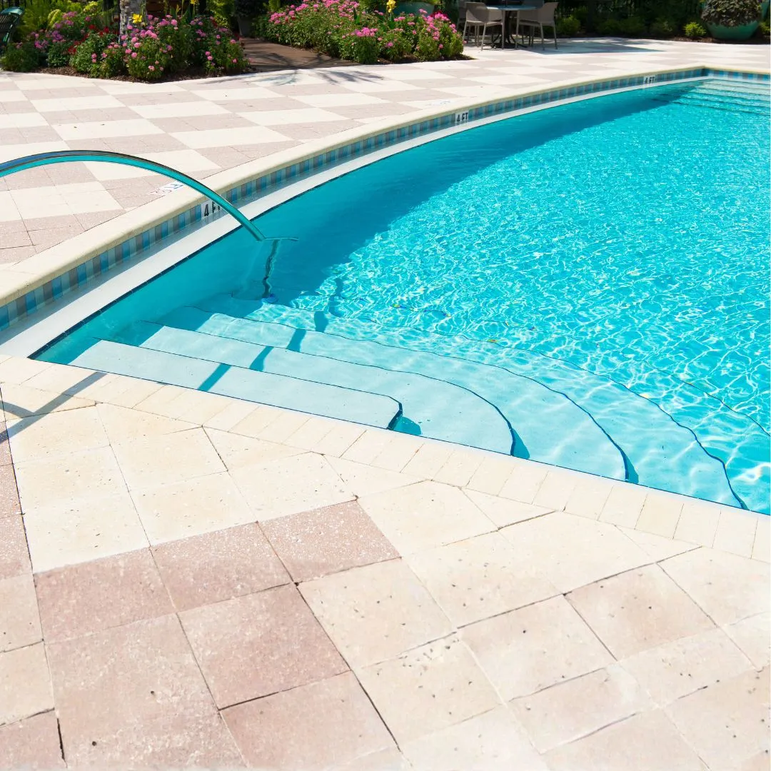 Custom curved inground swimming pool featuring clear blue water, light stone coping, entry steps, and stone paver patio surround in Raleigh, NC.
