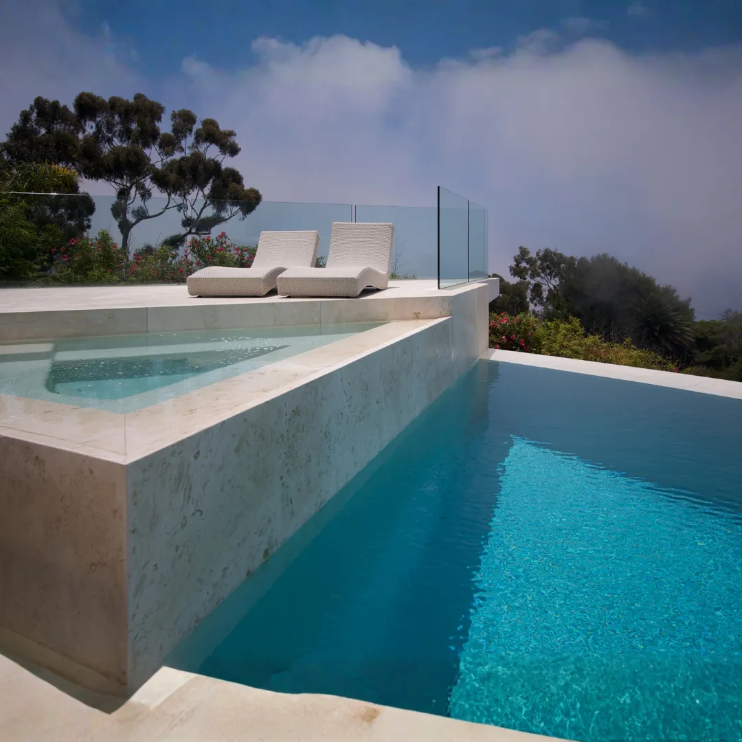 Modern white infinity plunge pool featuring clear blue water, clean architectural concrete walls, and built-in poolside lounge seating in Raleigh, NC.