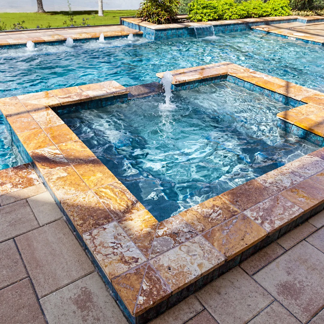 Custom inground swimming pool featuring a raised square stone spa with fountain spillways and stone paver patio coping in Raleigh, NC.