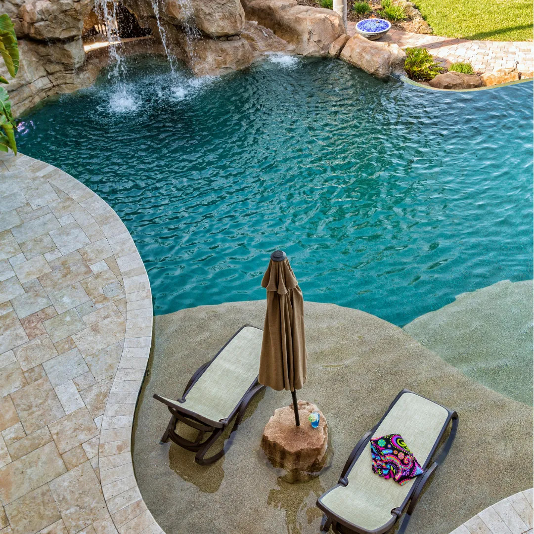 Custom lagoon-style inground swimming pool featuring a natural rock waterfall, stone patio coping, and poolside lounge seating in Raleigh, NC.
