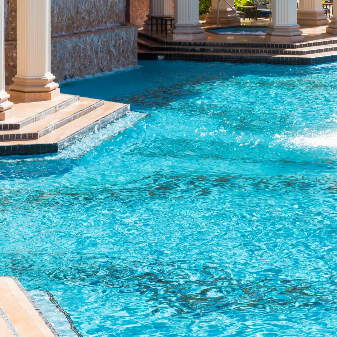 Luxury inground swimming pool featuring bright turquoise water, classical stone columns, and stone patio coping in Raleigh, NC.