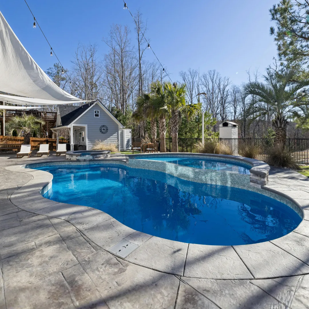Custom freeform inground swimming pool with deep blue water, stone paver patio surround, and lush backyard tree landscaping in Raleigh, NC.
